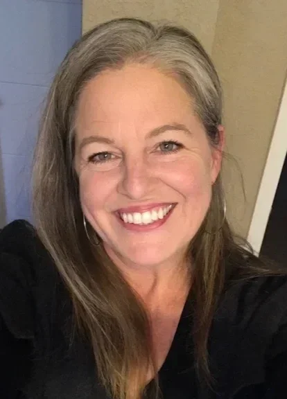 A woman with long gray hair smiling at the camera.