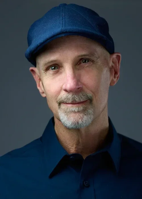 A middle-aged man with a light beard and mustache wearing a dark blue shirt and a blue cap.