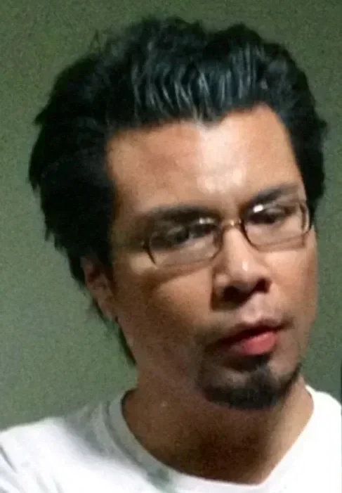 A man with dark hair, glasses, and a goatee looking at the camera with a serious expression.