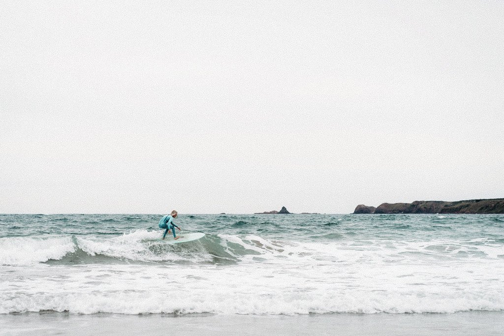 Person surfing on the ocean with waves and rocky coastline in the background.