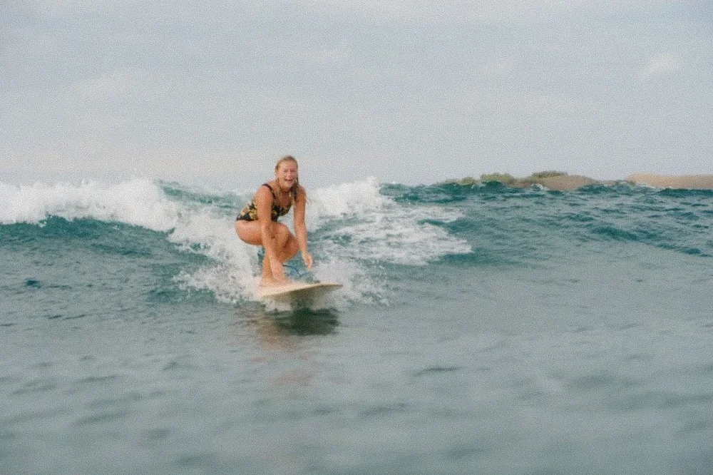A woman surfing on a wave in the ocean, smiling and crouching on her surfboard.