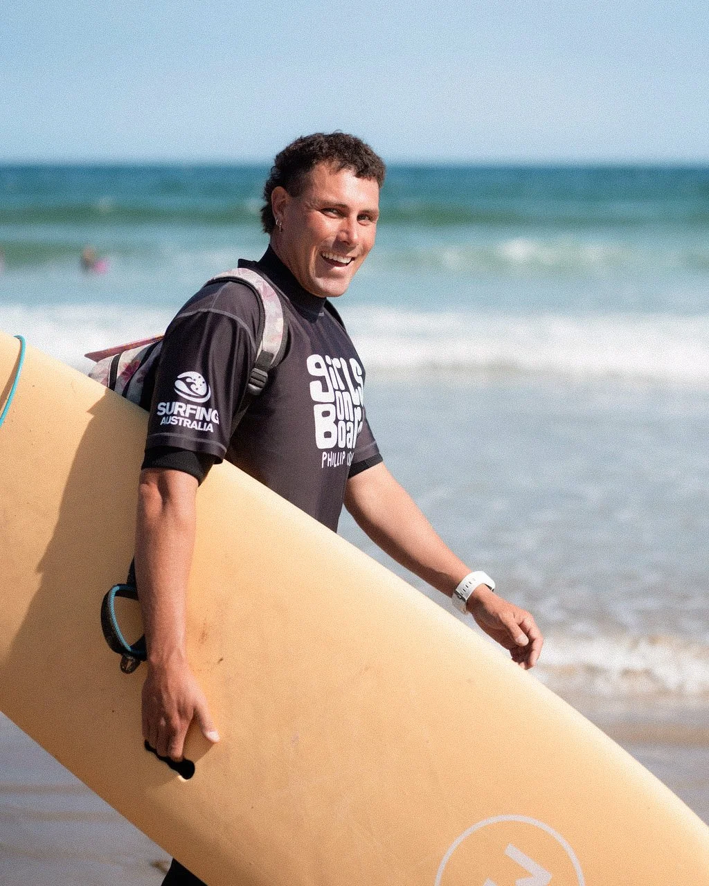 A man smiling and carrying a surfboard at the beach.