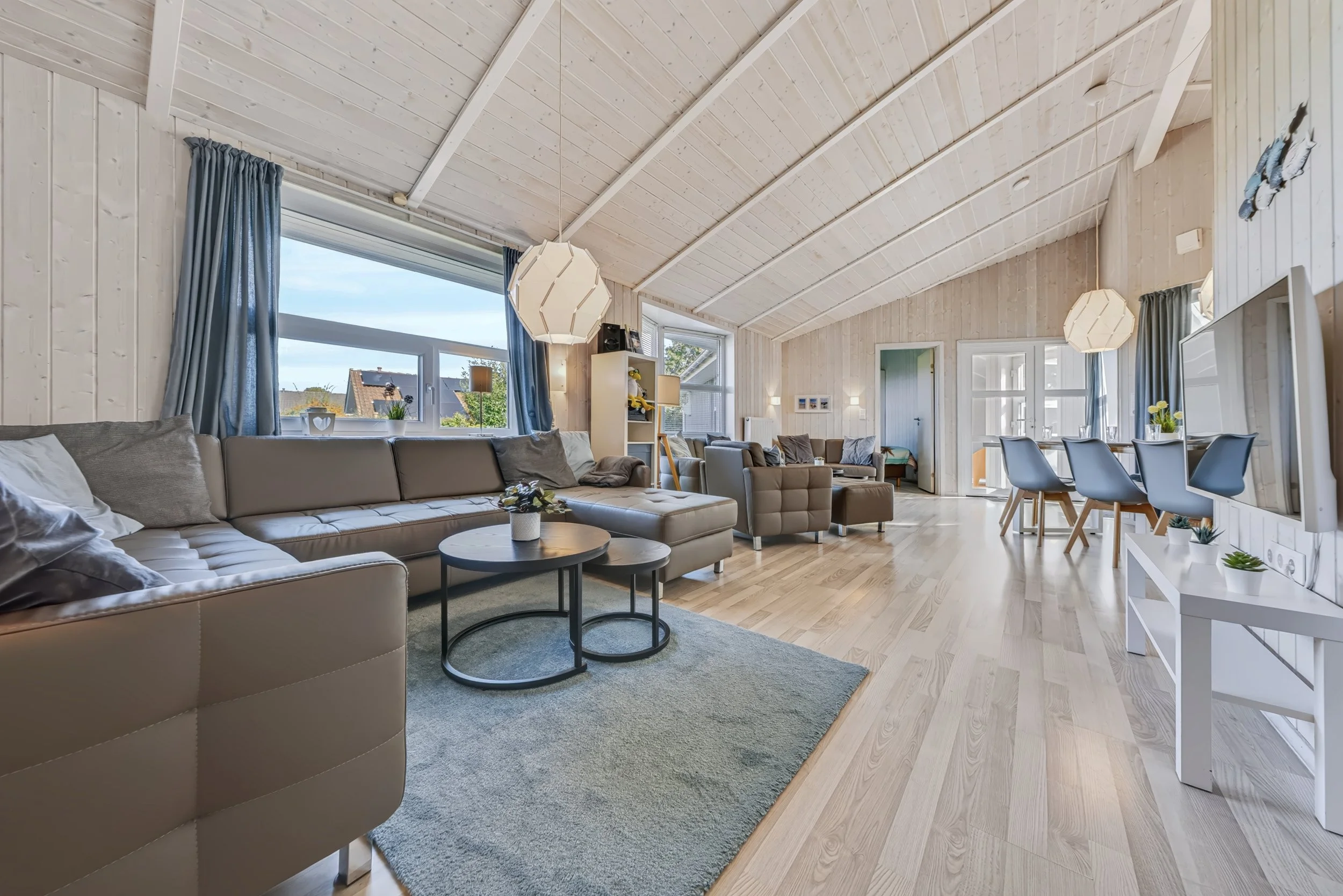 Wohnzimmer mit hoher Holzdecke
Großzügiger Wohnbereich in The Lazy Möwe mit hoher Holzdecke und großen Fenstern
