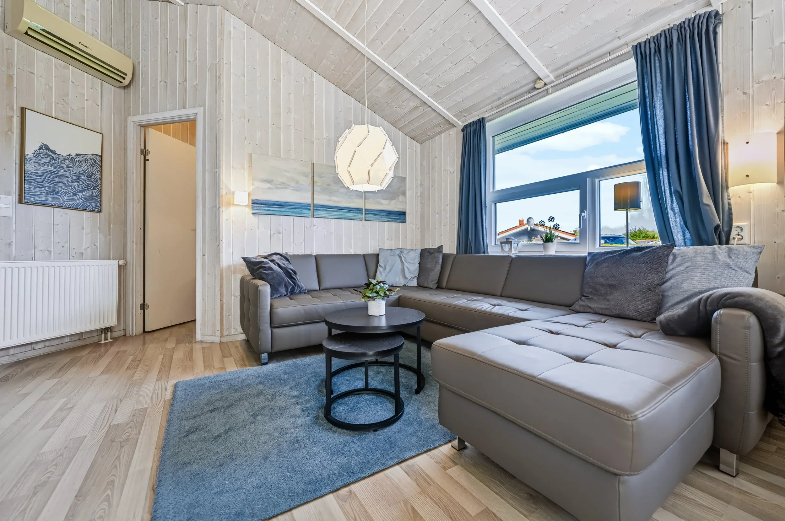 Wohnzimmer mit maritimer Wandkunst
   Heller Wohnbereich in The Lazy Möwe mit Sofa, Klimaanlage und maritimer Wanddekoration