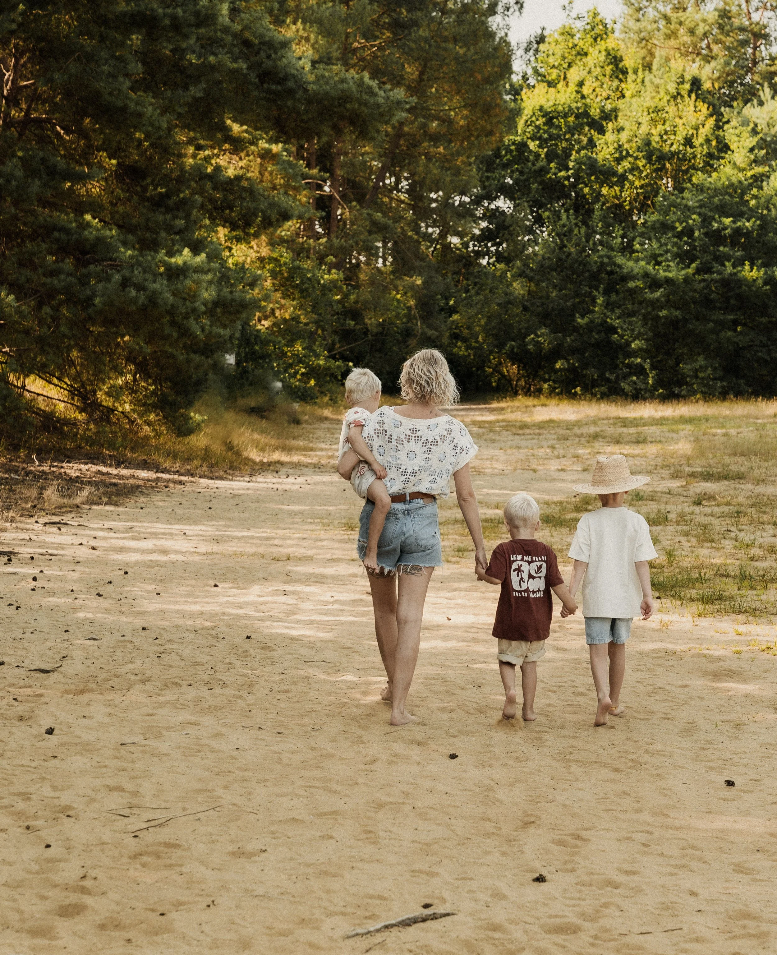 Mama wandelt hand in hand met haar drie kinderen over een zandpad in het bos, gezinsfotografie in de Kempen