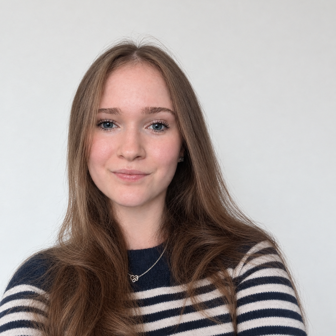 Young woman with long light brown hair, wearing a striped navy and white sweater, smiling softly, standing against a plain white background.