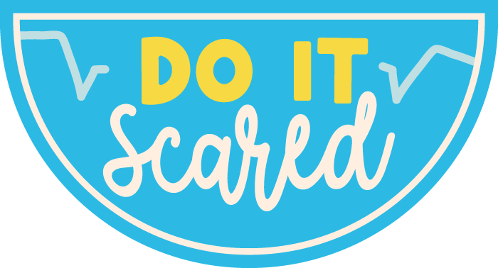 A sign with a light blue background and a white border featuring the phrase "Do It Scared" in bold yellow and white letters, with line graphs in the background.