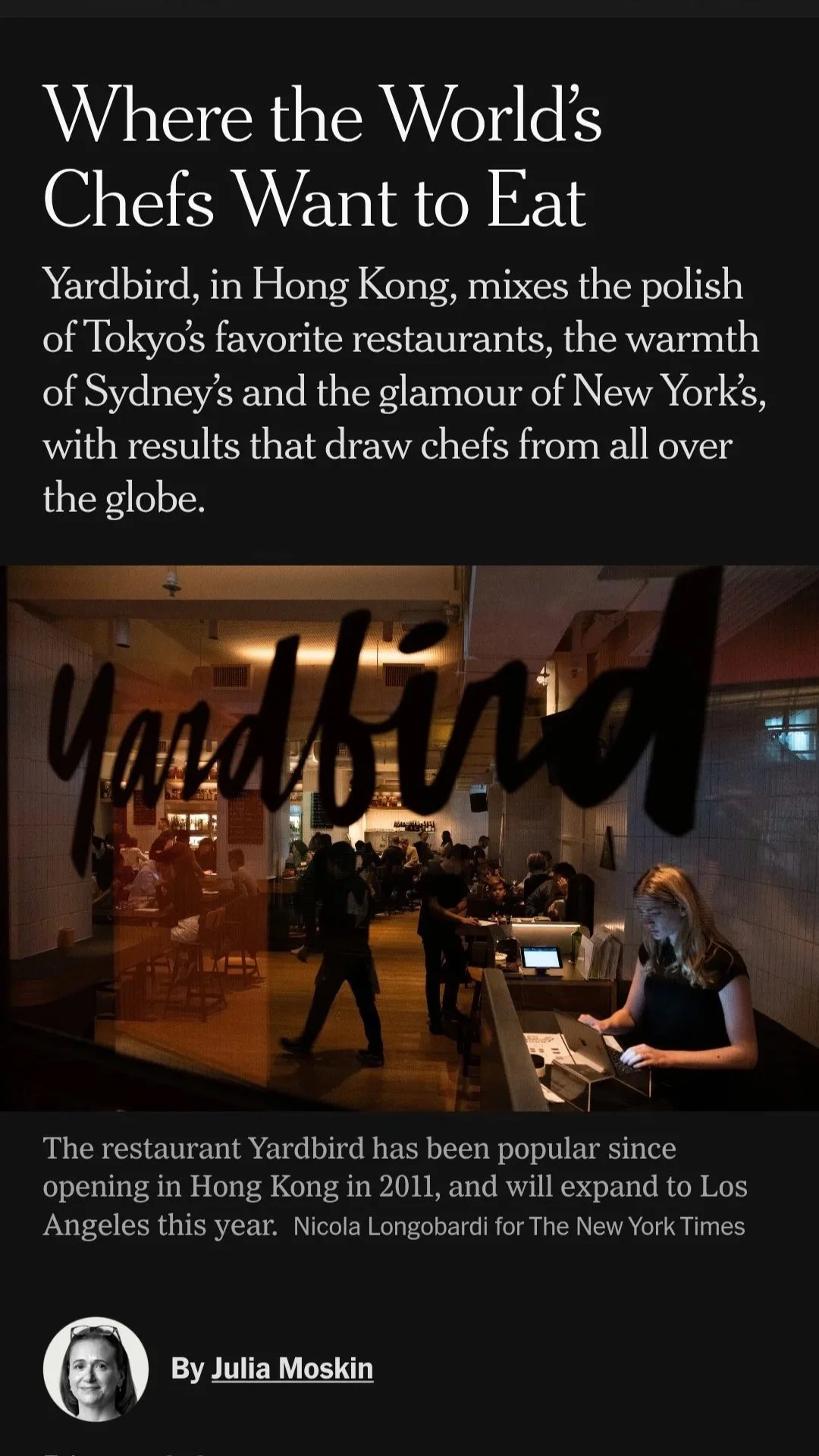 A photo of the interior of the restaurant Yardbird, seen through a glass window with the word 'Yardbird' written on it. Inside, people are dining and a woman is working at the counter.