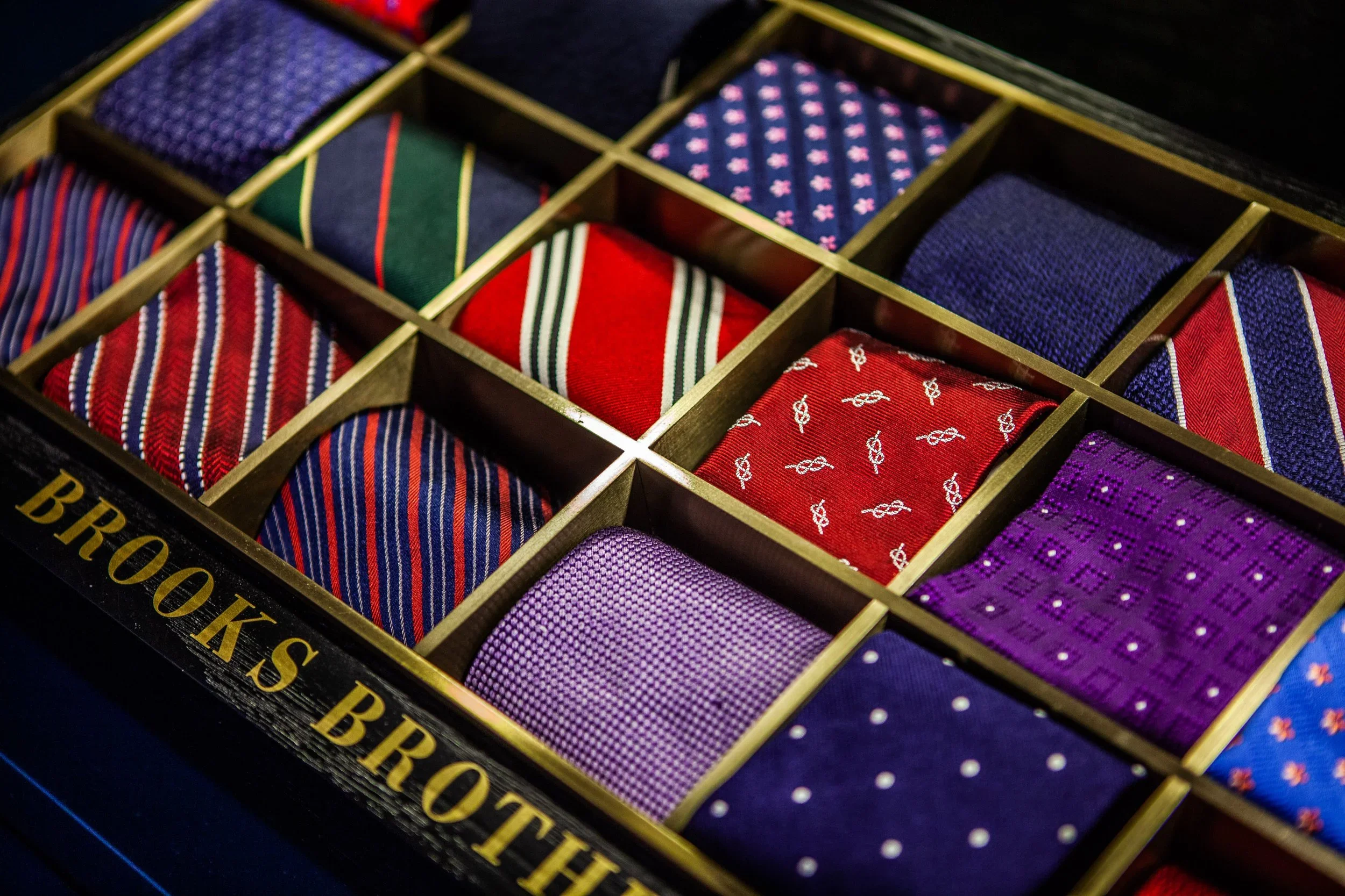 A box of assorted men's neckties with various patterns and colors arranged in a grid formation.