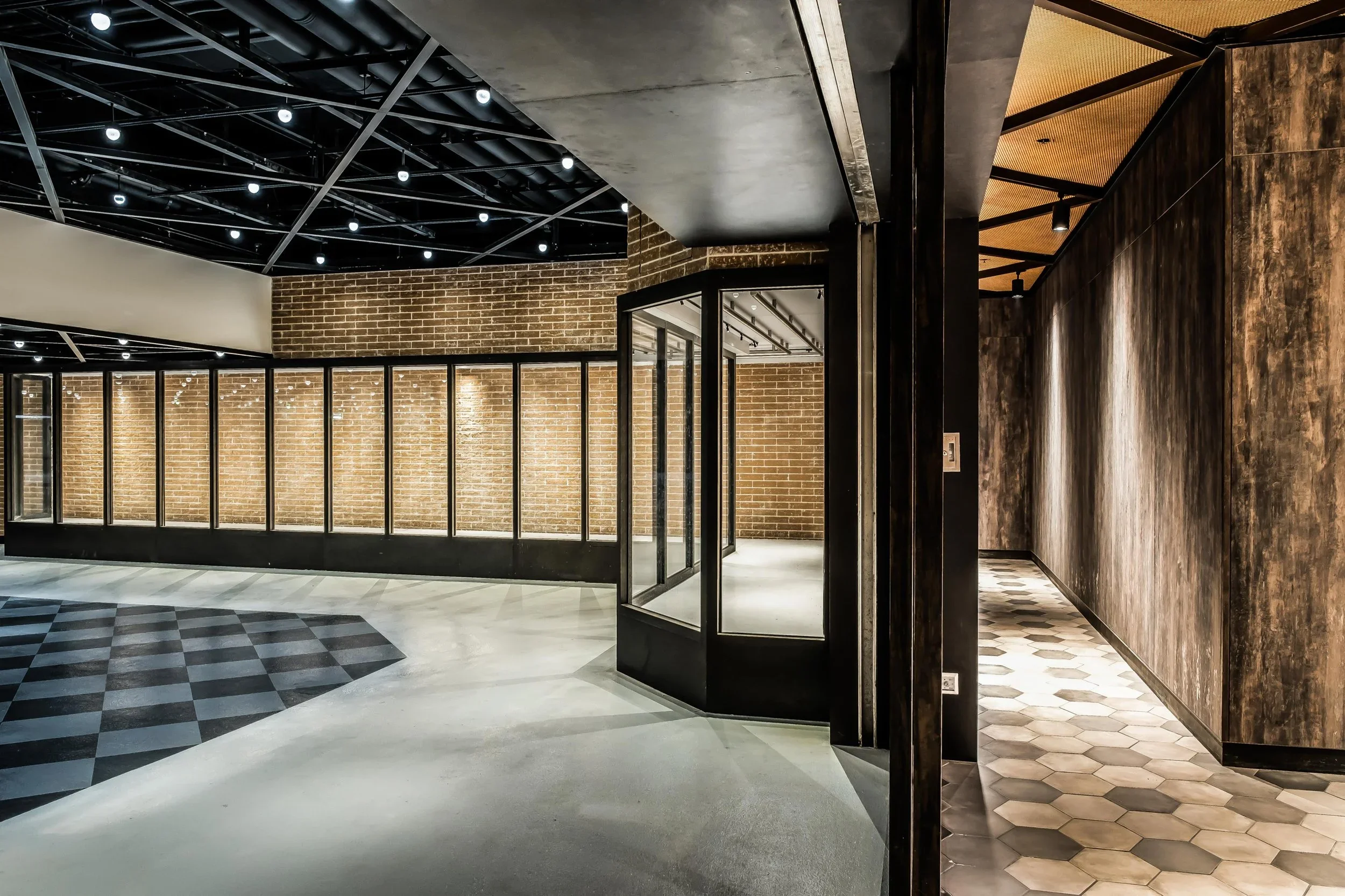 Interior of a modern building with brick walls, black ceiling with small white lights, a glass partition, and a mix of patterned flooring.