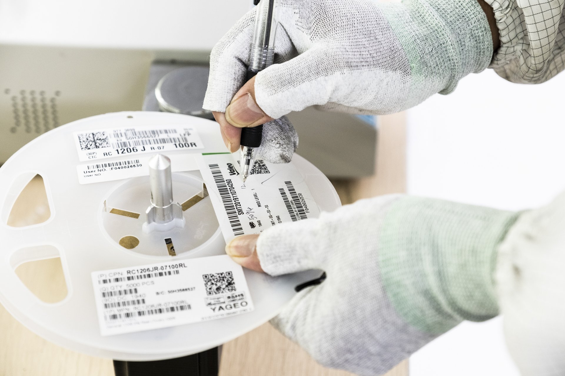 Person wearing gloves handling a spool of labeled medical or laboratory tape or labels, with a pen marking on one of the labels.