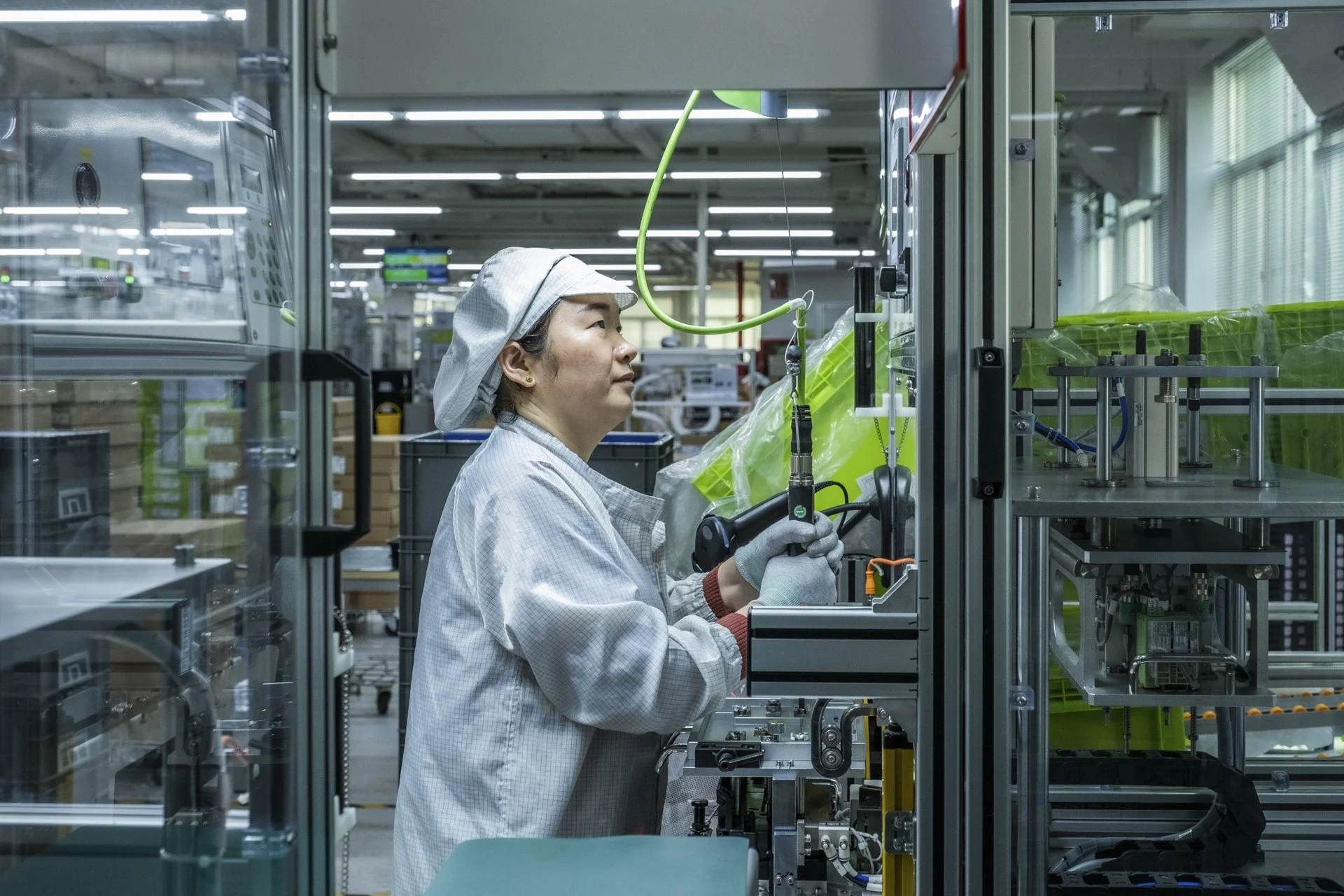 A woman working in a cleanroom, wearing protective clothing and handling equipment inside a laboratory or factory setting.