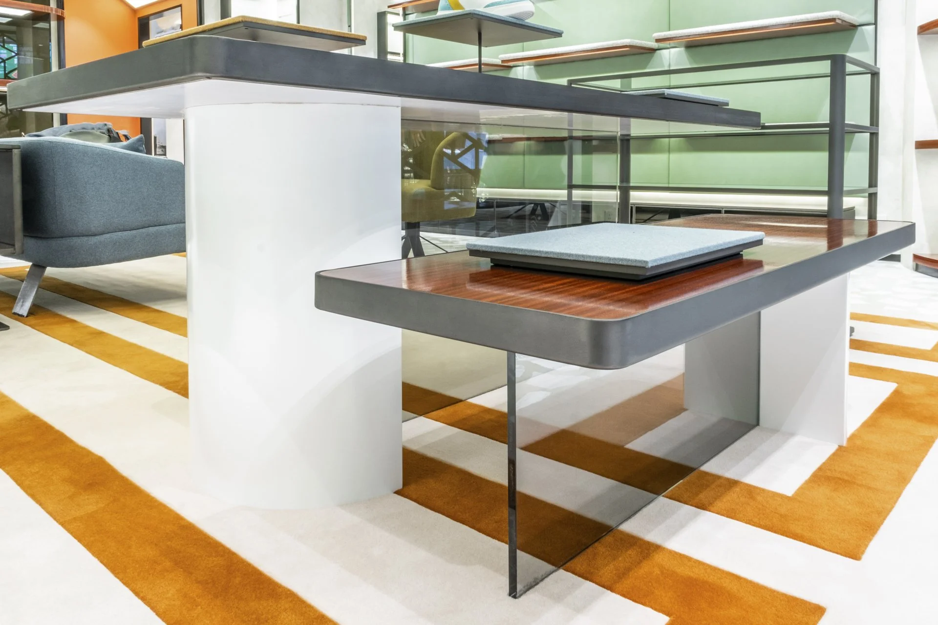 Modern interior workspace with a multilevel glass and wood desk, colorful walls, and a patterned carpet.