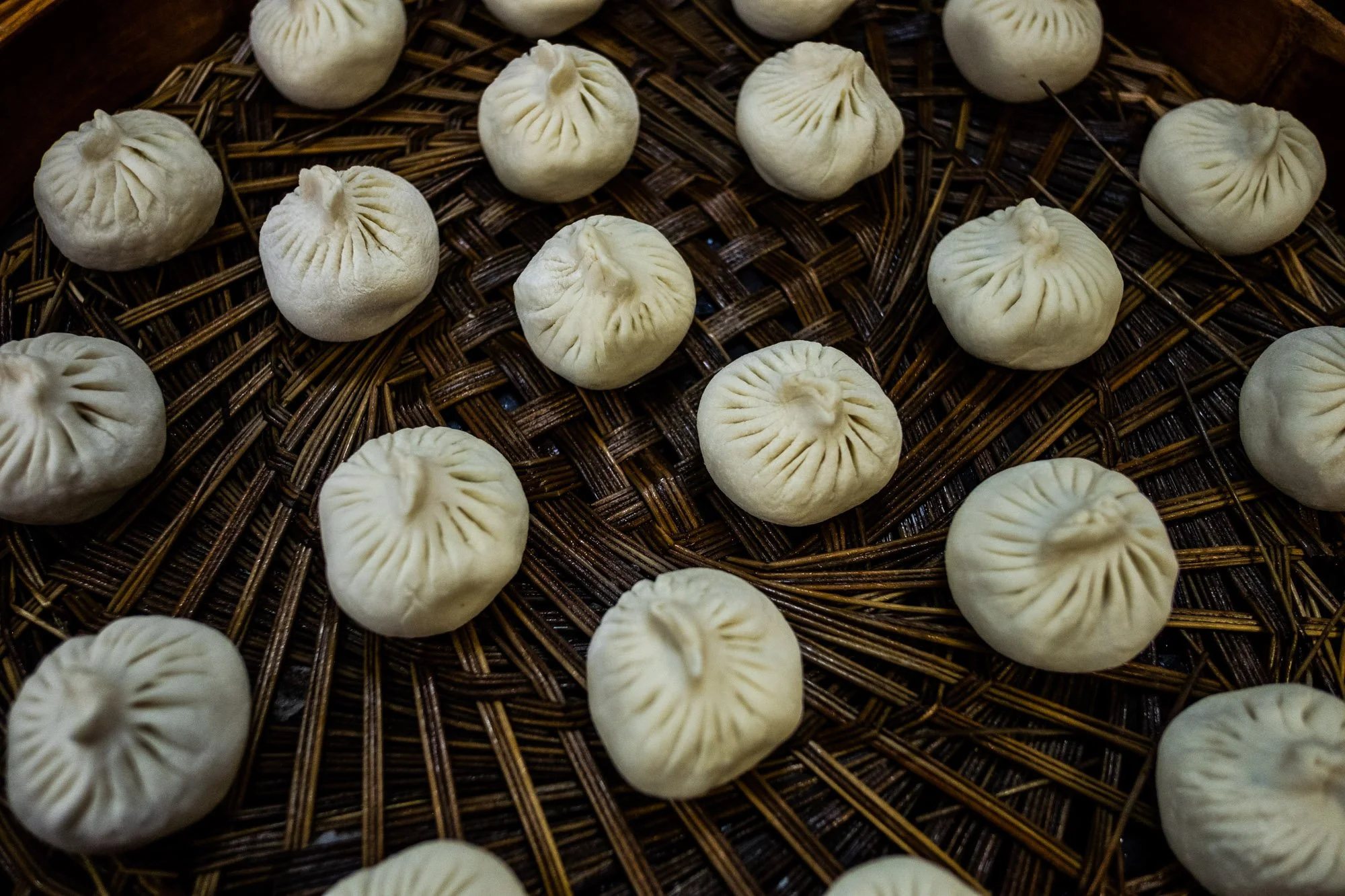Multiple steamed dumplings arranged on a woven bamboo tray.