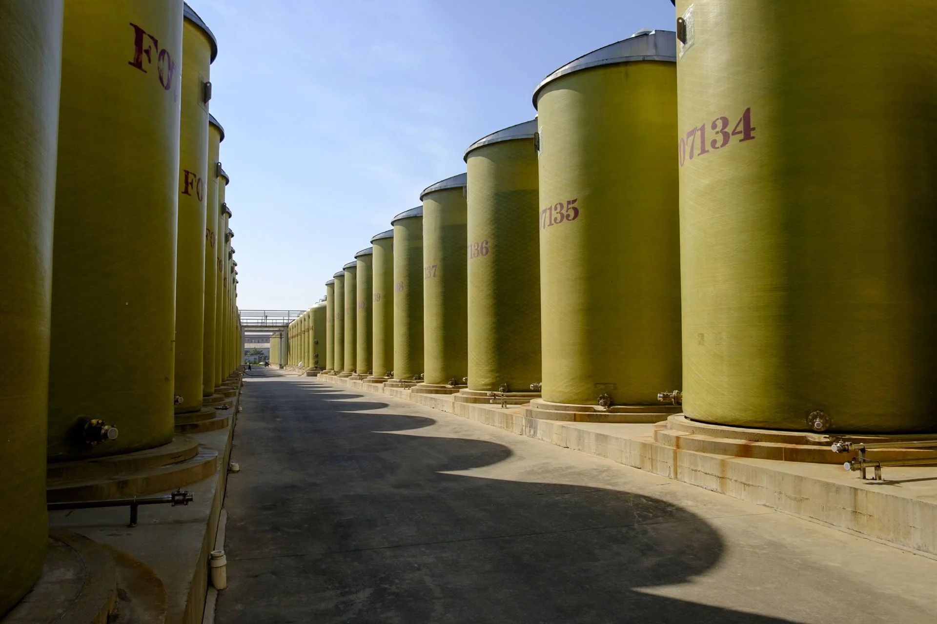 Several large yellow industrial storage tanks lined up outdoors on concrete bases under a clear blue sky.