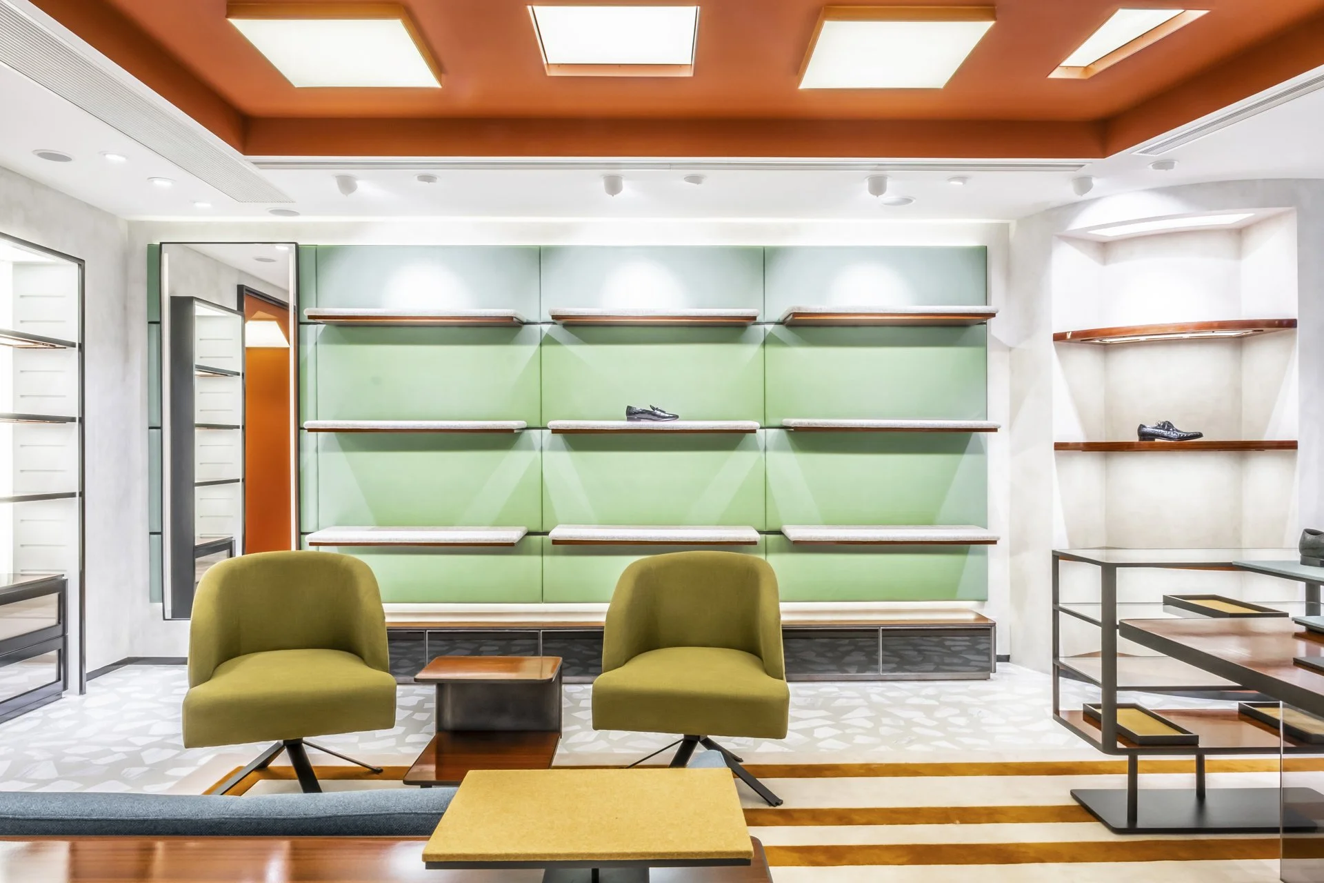 Interior of a modern store or waiting area with green and white wall panels, shelves displaying shoes, and green armchairs in the foreground.