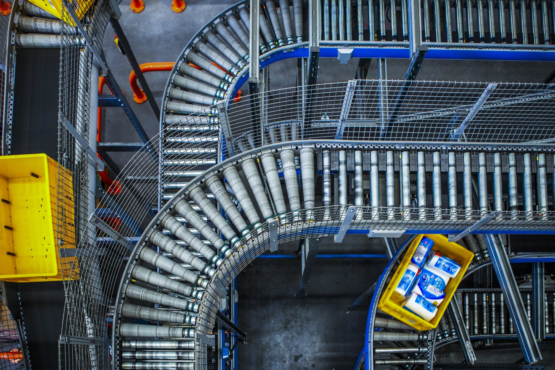 Overhead view of a warehouse or industrial storage area with metal shelves, yellow bins, and a conveyor system.