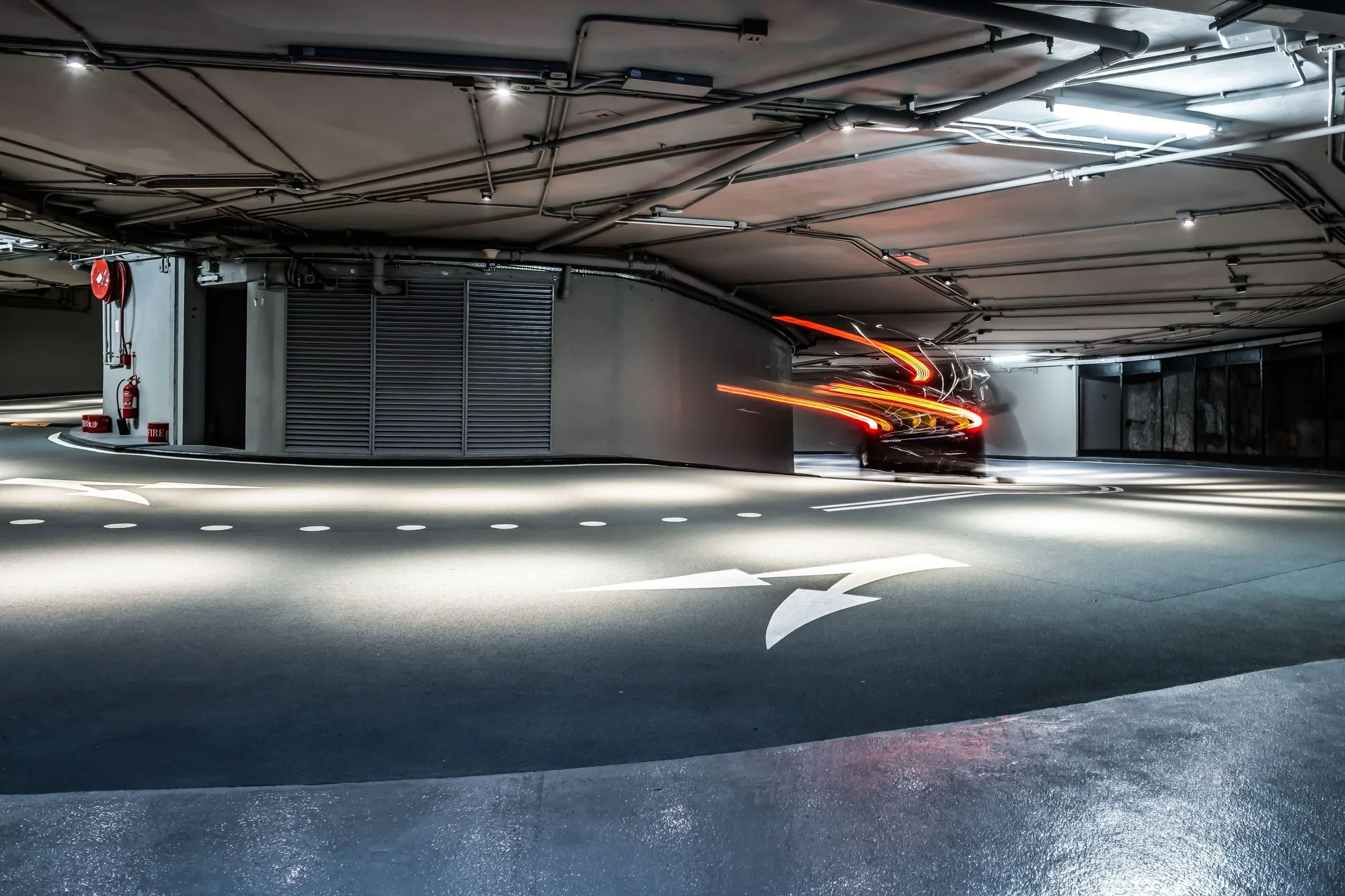 Moving car in an underground parking garage, with light trails from its taillights.