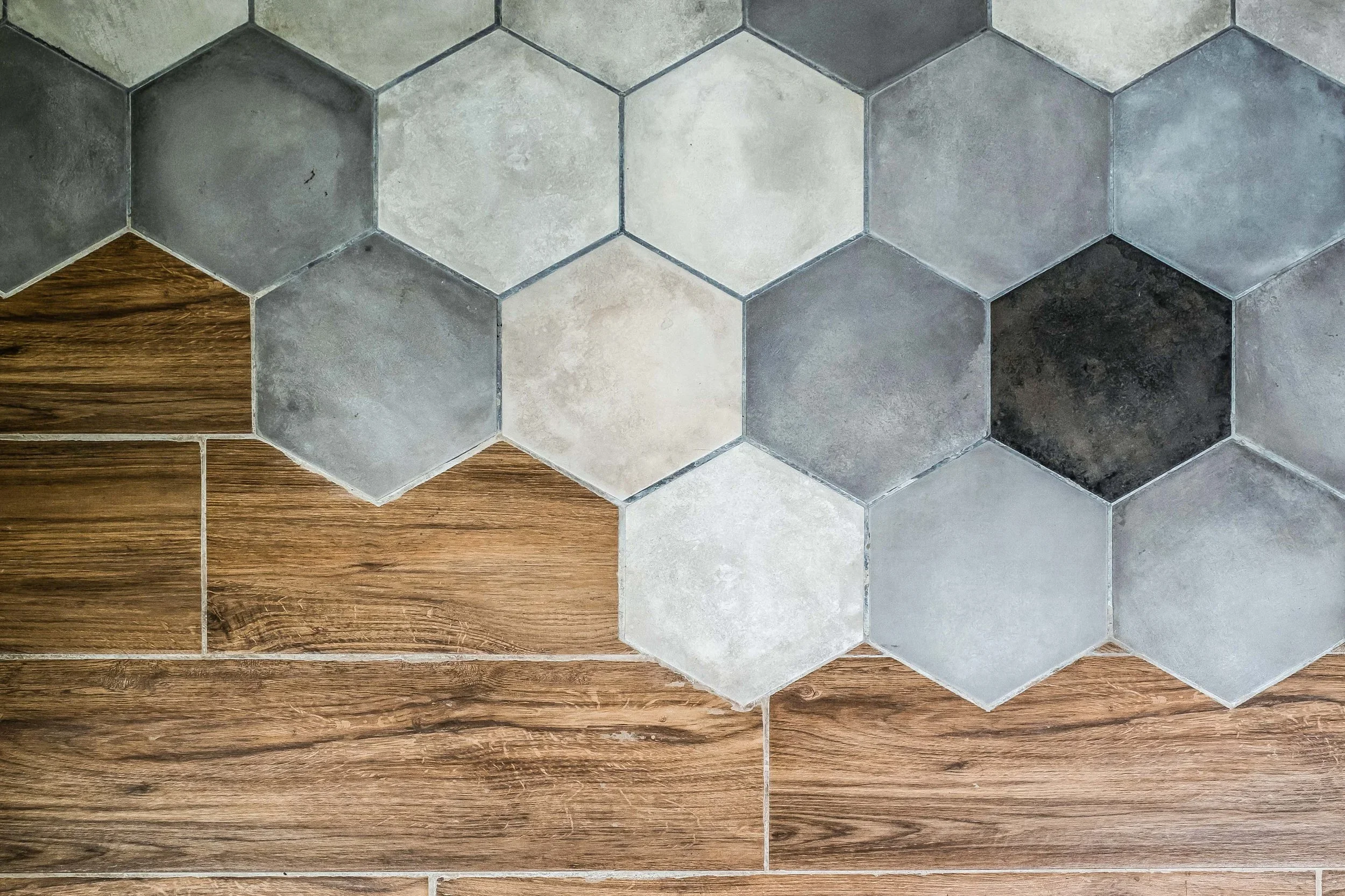 Close-up of wooden flooring and hexagonal tiles in shades of gray.