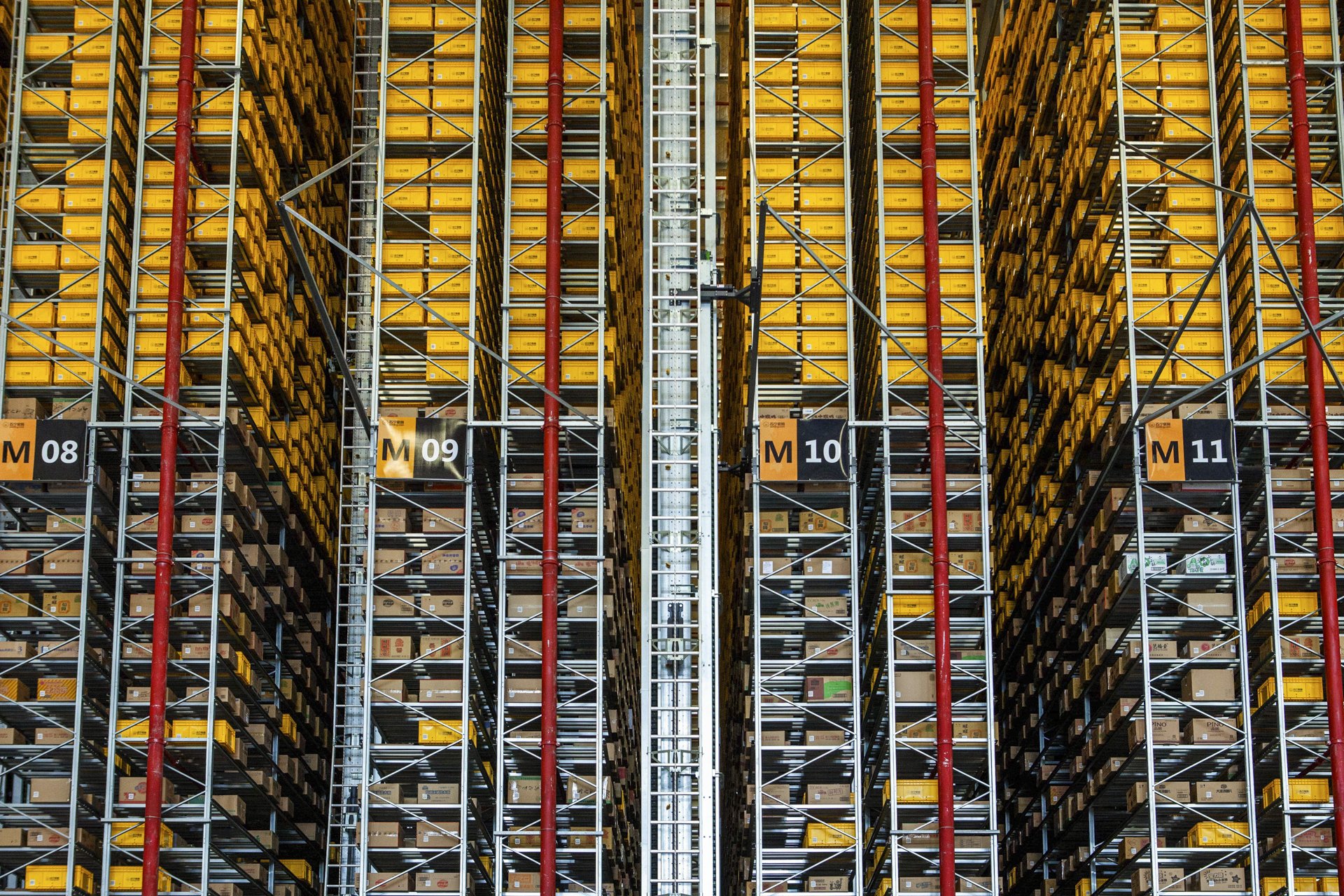 Tall warehouse shelves filled with yellow bins, numbered M08 to M11, supported by metal and red pipes.