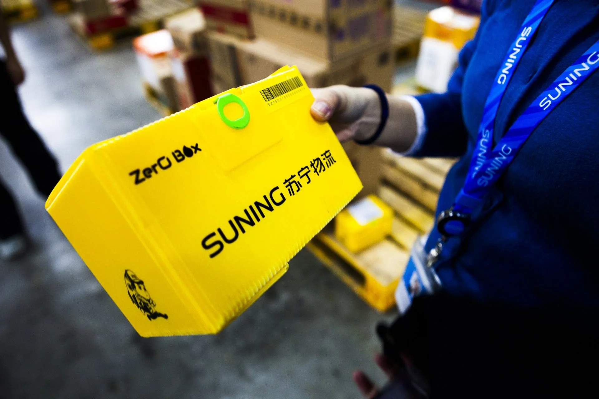 Person holding a yellow box labeled 'Zero Box' and 'Suning' in a warehouse or store with shelves of products.