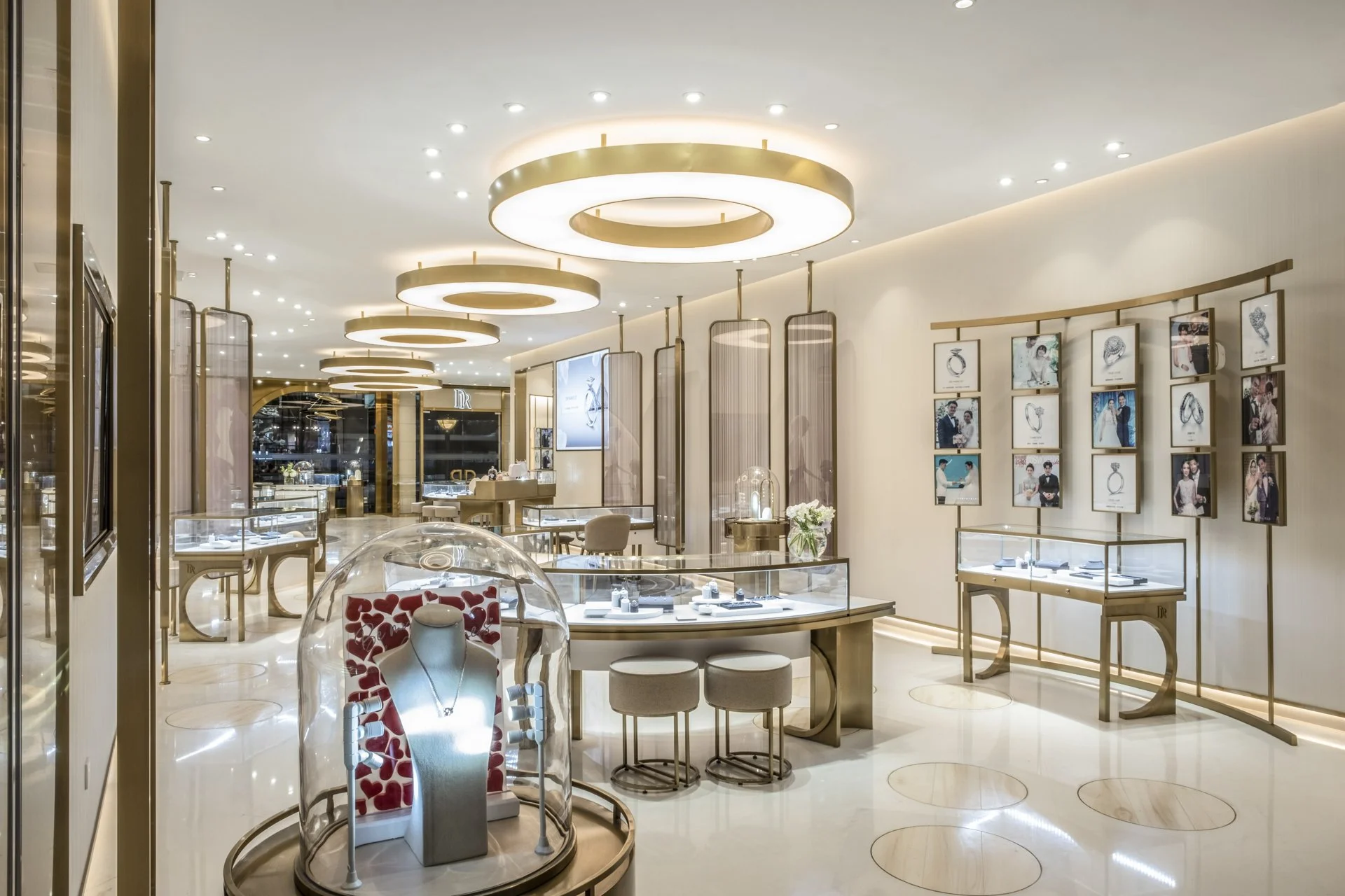 A jewelry store interior with modern design, featuring circular ceiling lights, display cases with jewelry, and framed photos of models wearing jewelry on the wall.