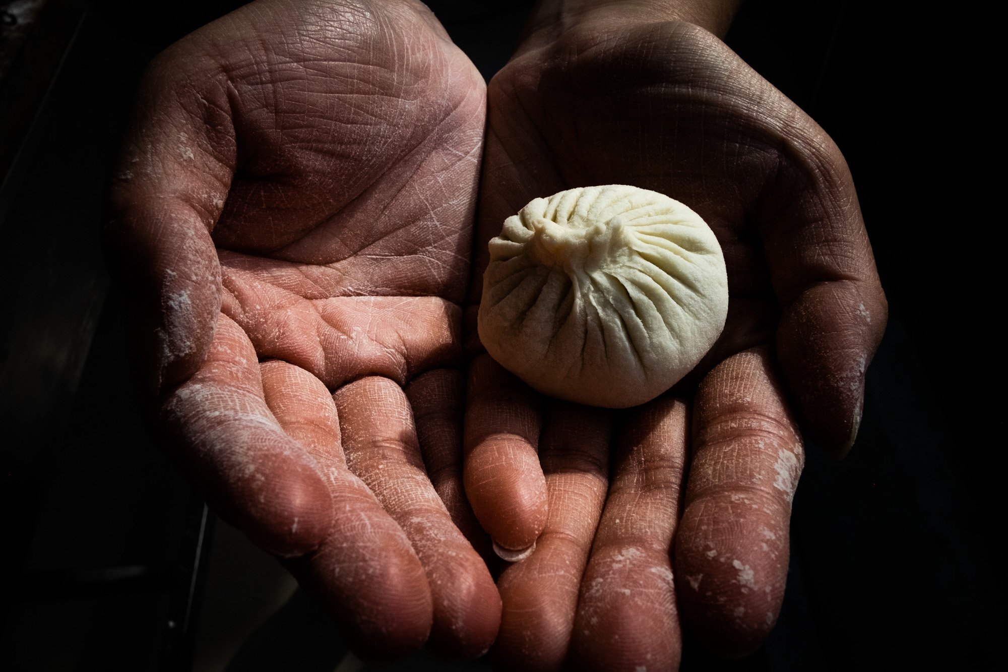 Close-up of two hands holding a small, round tea leaf dumpling with pleated edges.
