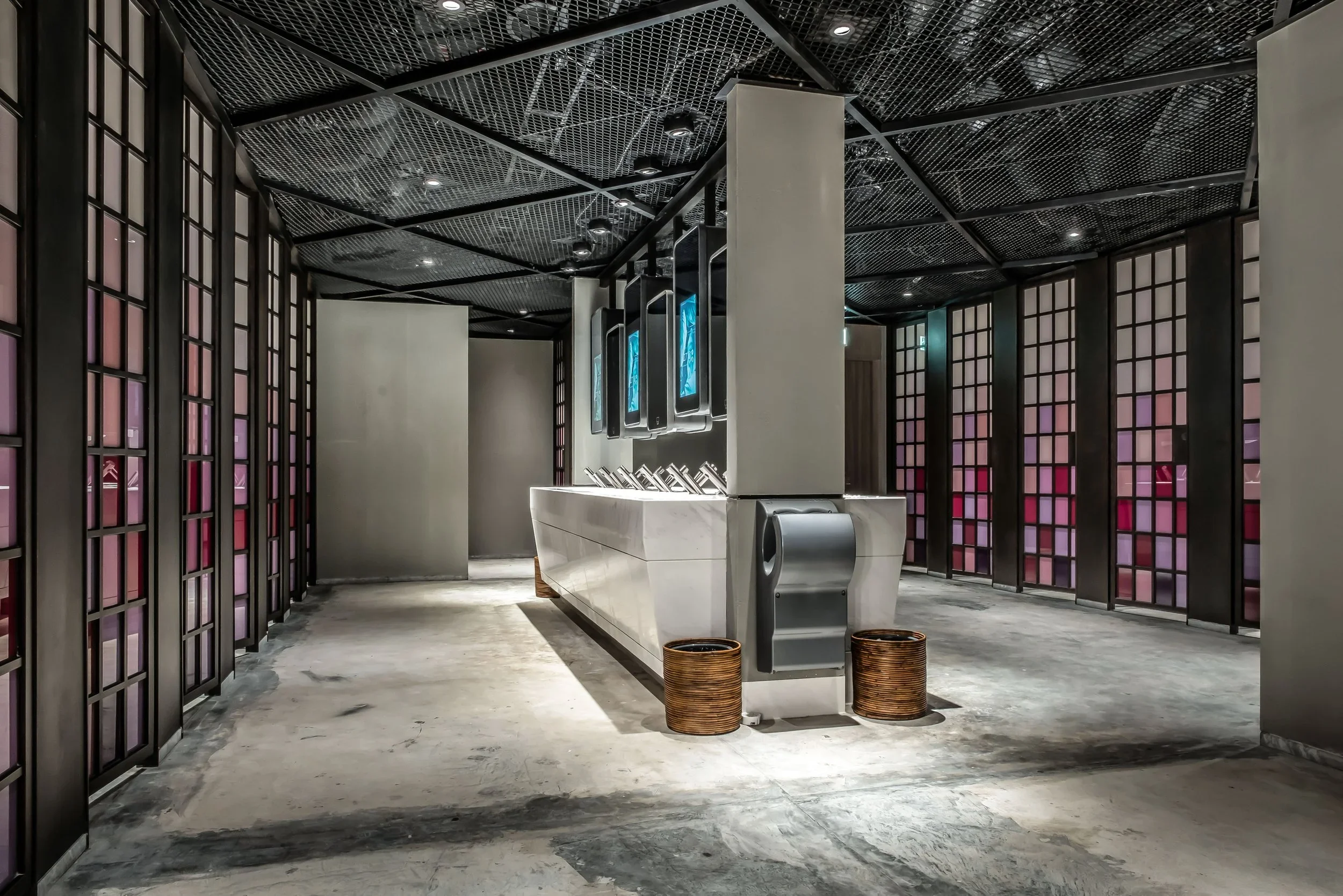 Modern interior with dark metal ceiling, black lattice walls with purple panels, marble reception desk, digital screens, trash bins, and minimal decor.