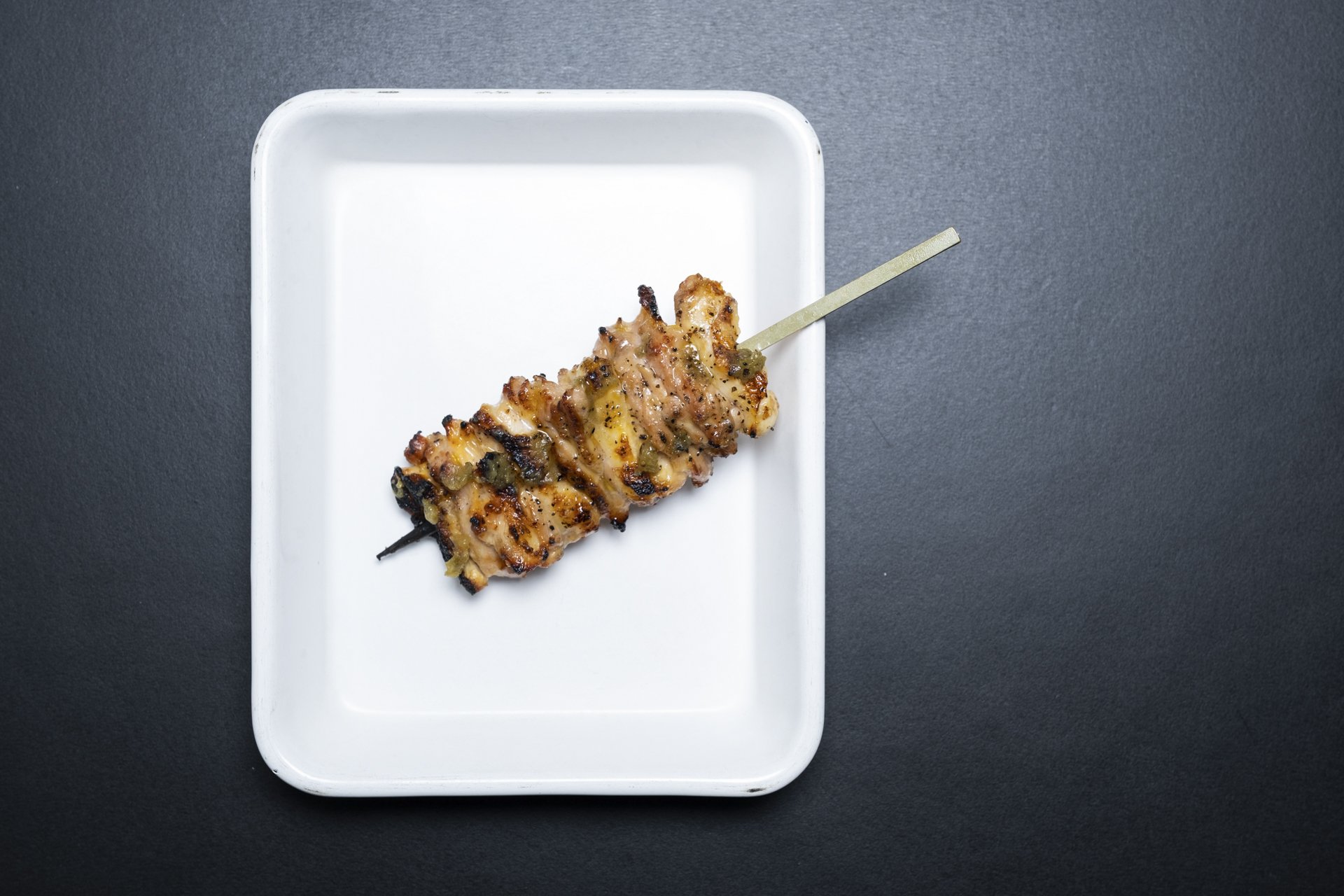 Grilled chicken skewer with herbs on a white rectangular plate on a black surface.