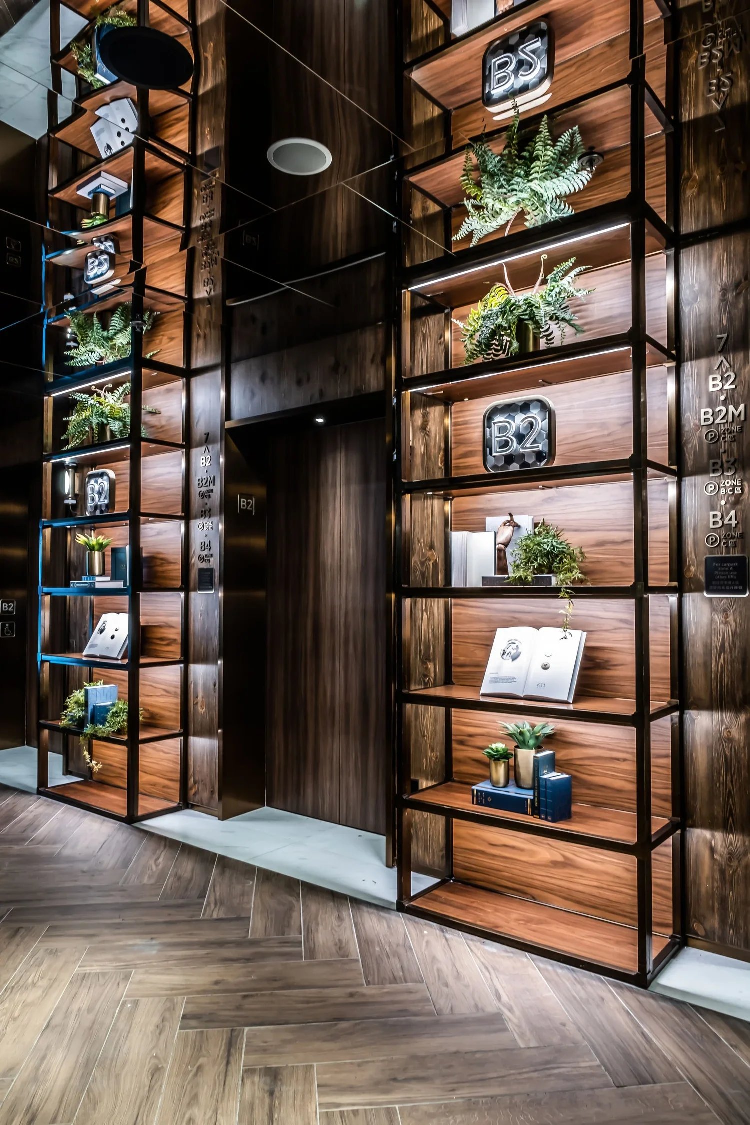 Interior of a modern building with wooden and black metal shelves decorated with green plants, books, and decorative objects.