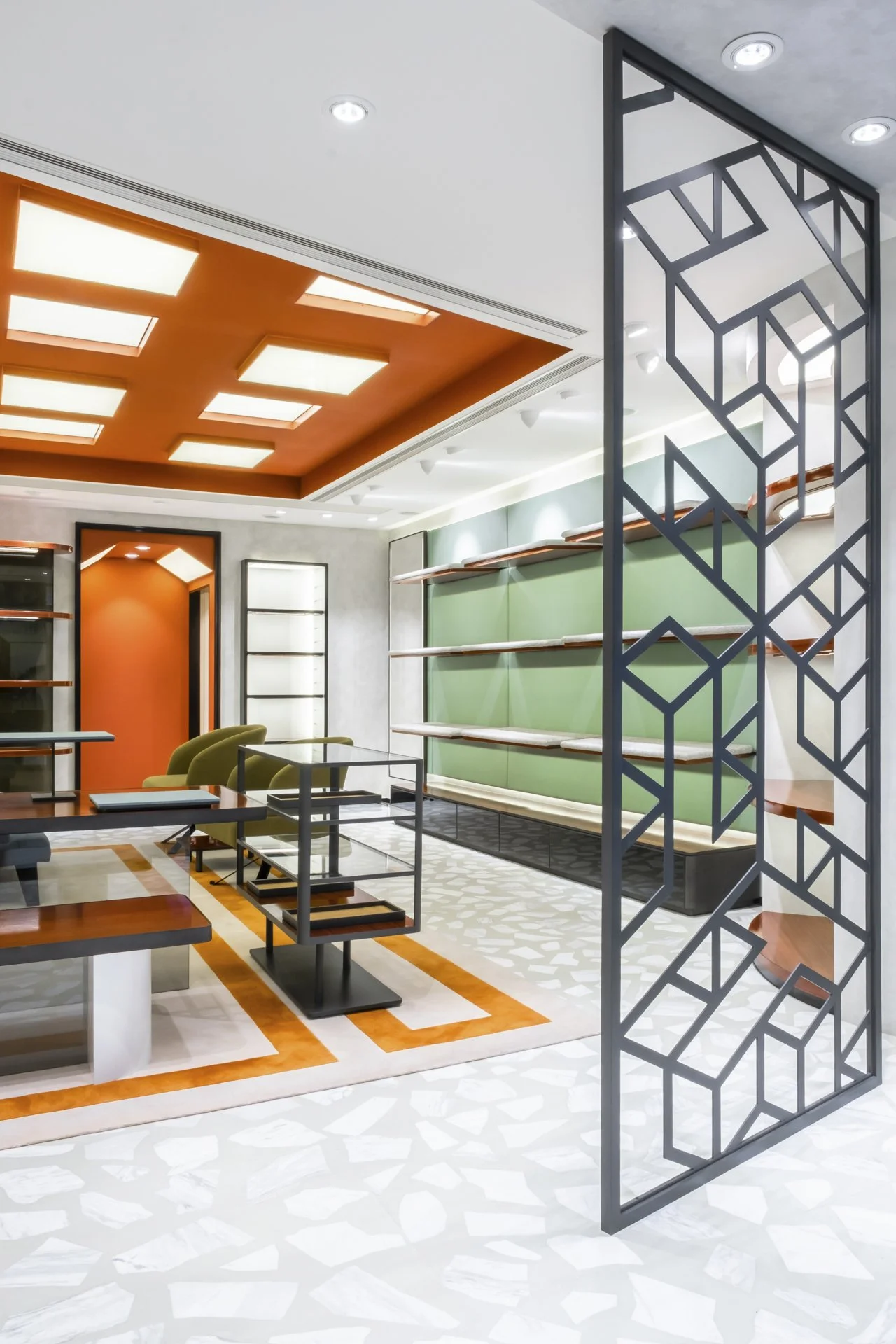 Modern interior living space with ceiling lights, an orange ceiling, green wall with shelves, patterned floor, and decorative black metal room divider.