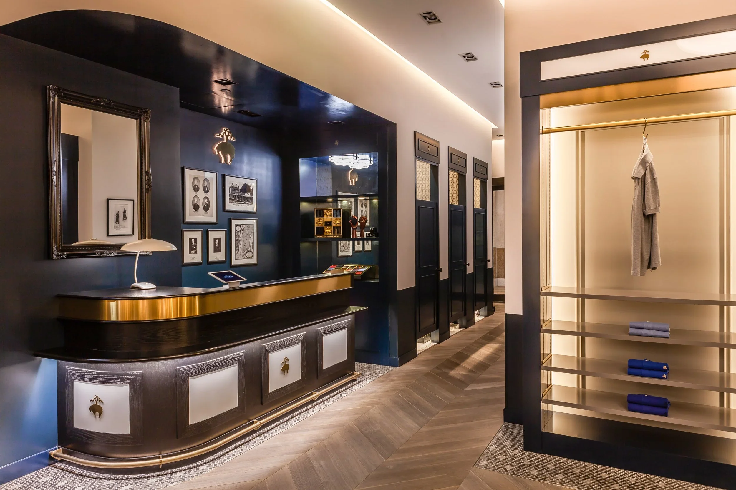 Interior of a stylish shop with a dark and light color scheme, framed photographs on dark blue walls, a curved counter with a gold trim, and a clothing display area with shelves.