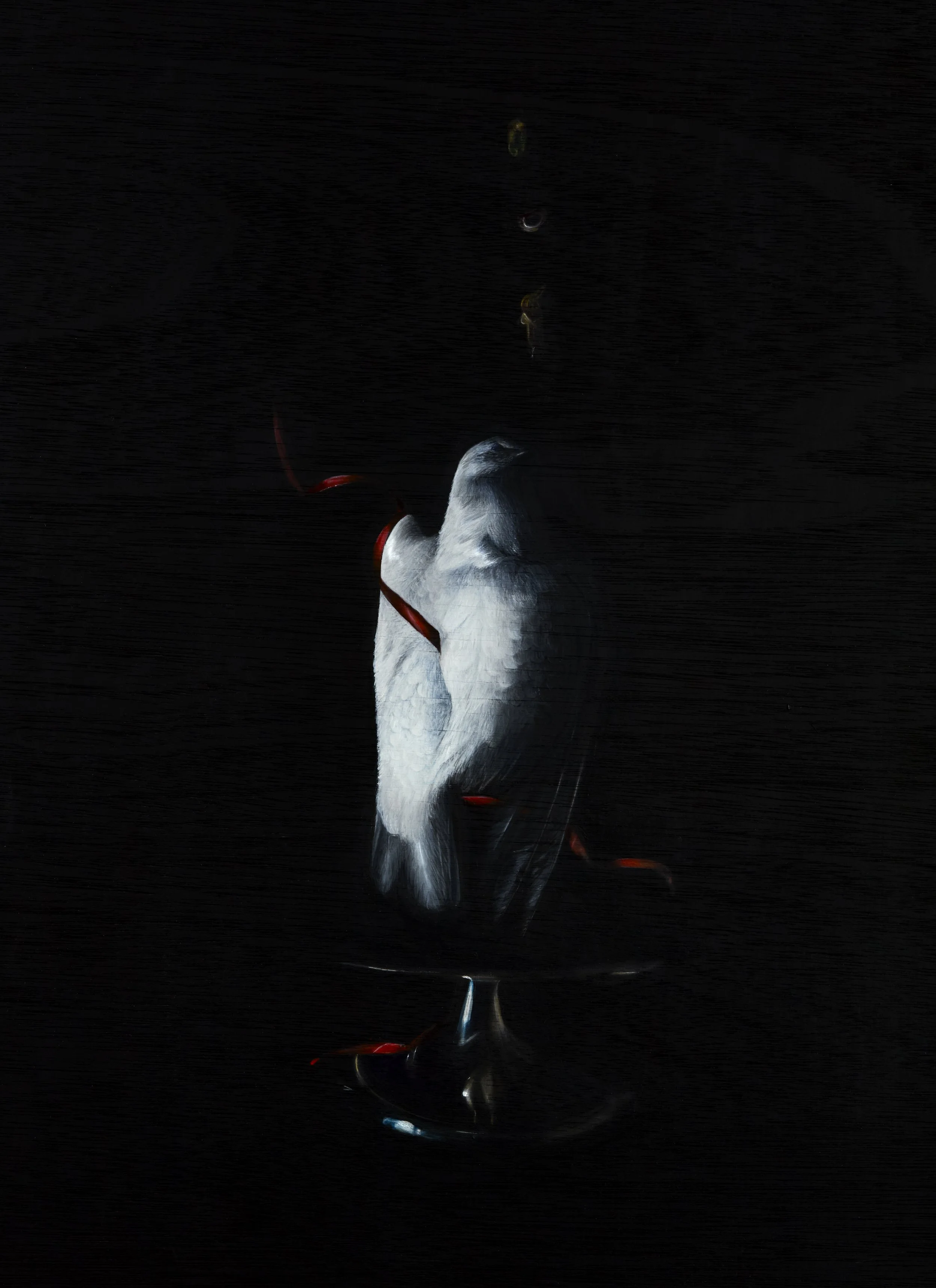 A white dove on a wine glass cake stand with a dark background, and a red ribbon around its neck, illuminated softly.