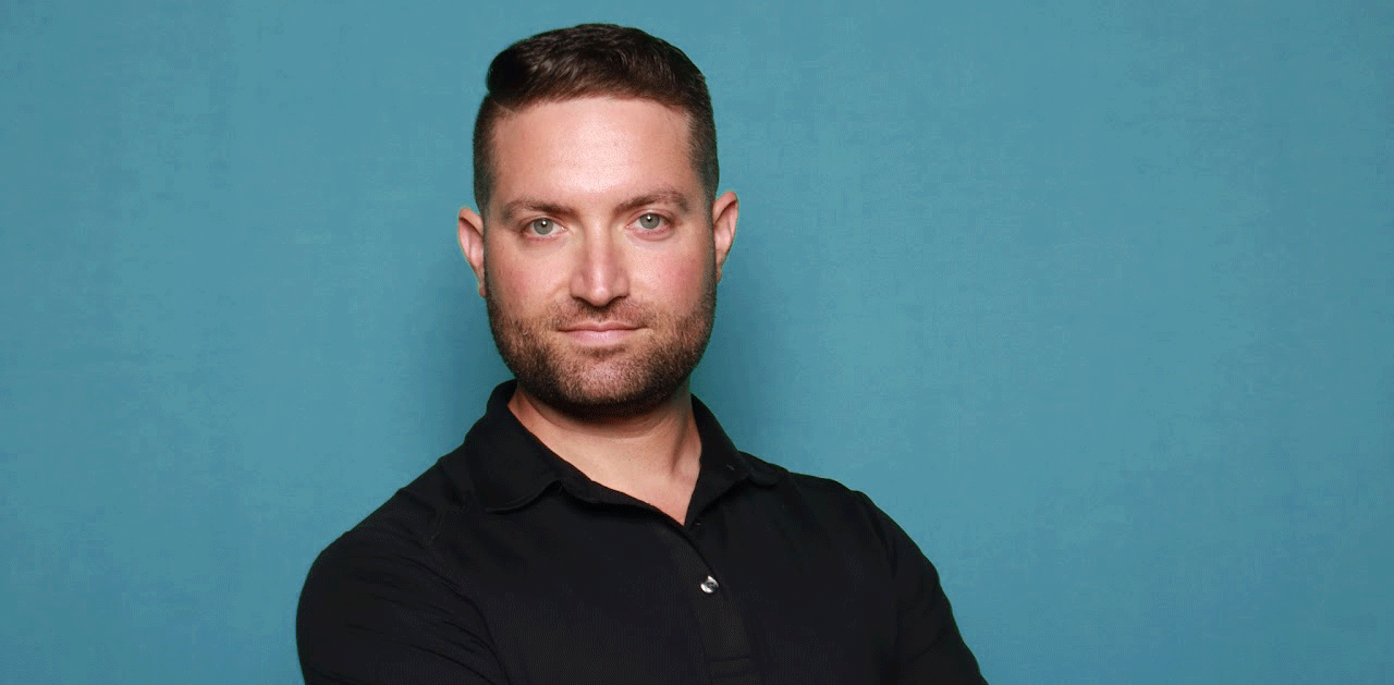 Photo of Bryce Griffler, a white male with brown hair, blue eyes and a brown beard, on a teal backdrop