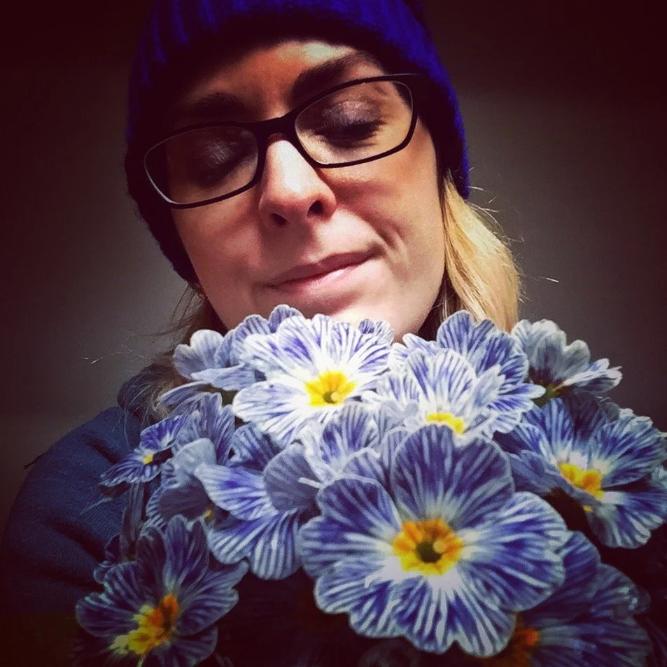 Portrait photo of Joanna Ritchie smelling a bouquet of pretty blue flowers.