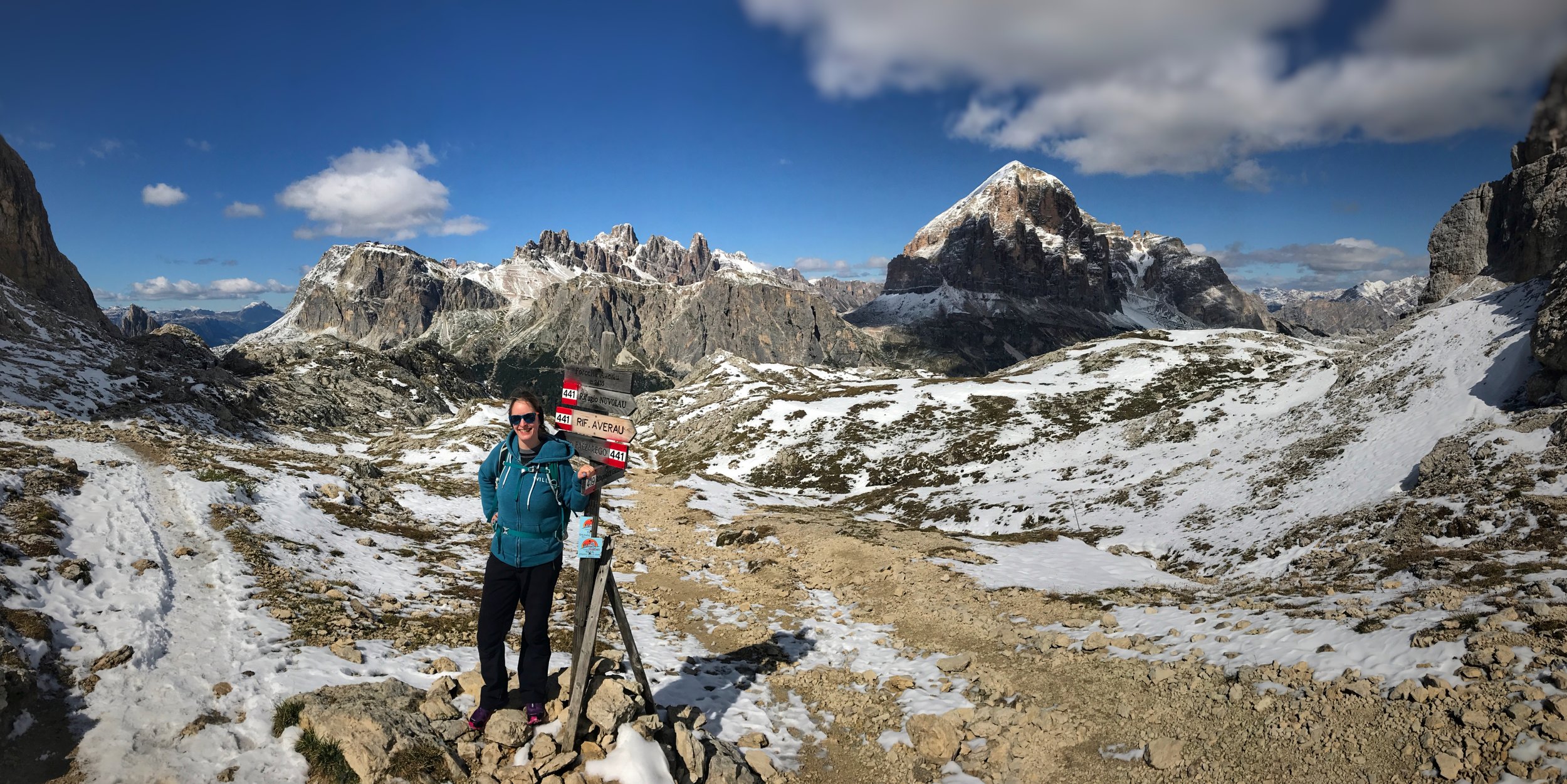 Landscape photo of Joanna Ritchie standing at a sign in the heart of the snow capped Dolomite mountains in Italy.