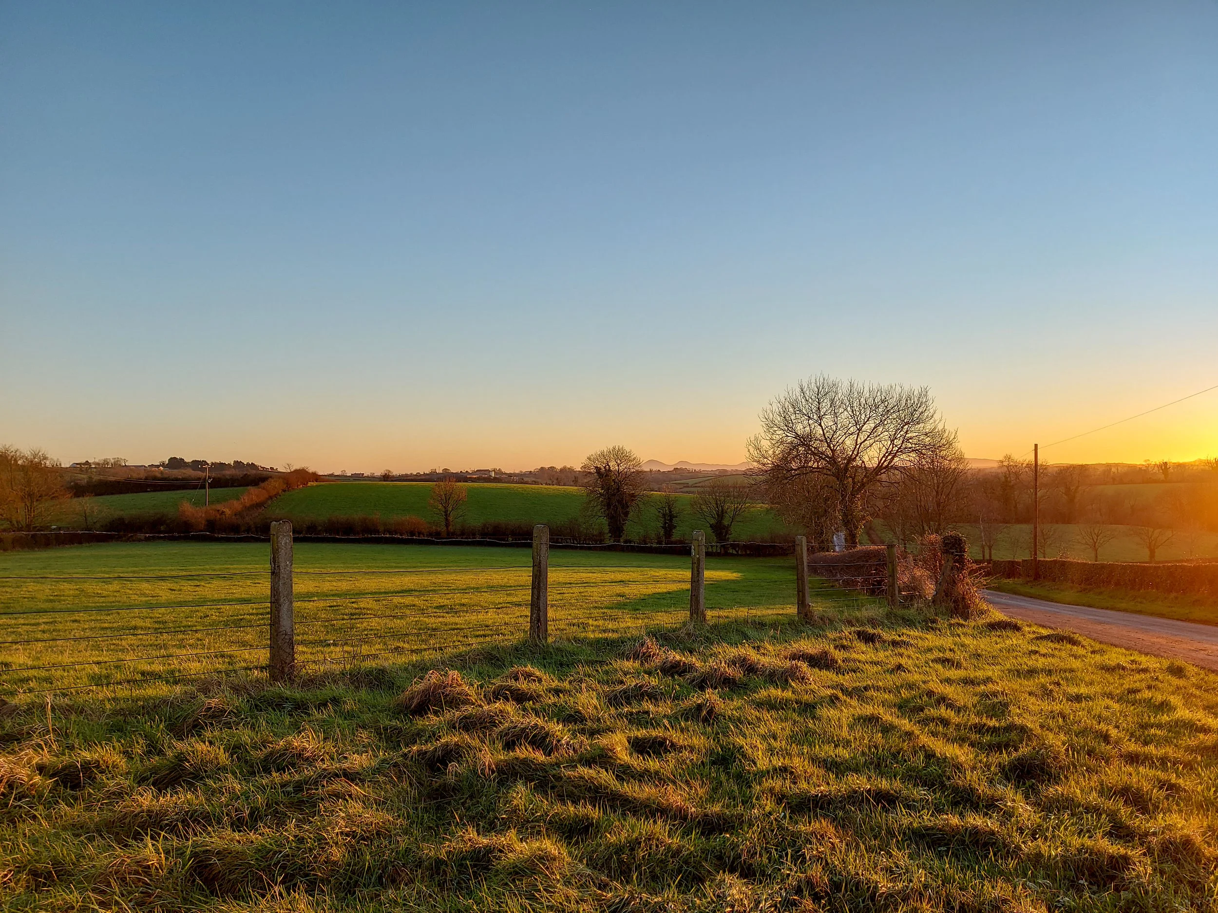 Landscape photo of a sunset over green fields with a view of the Mourne Mountains in Northern Ireland.