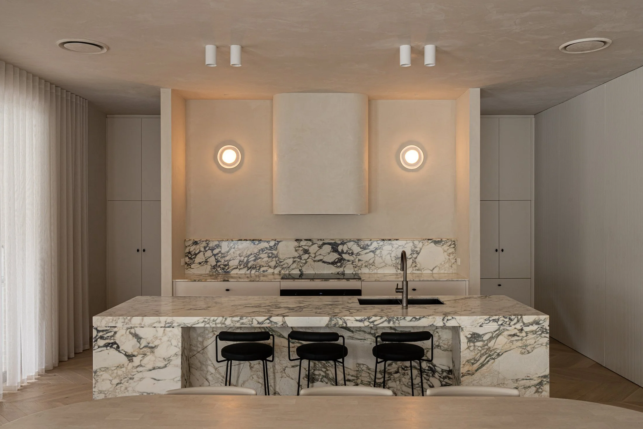 St Morris kitchen with a veined stone island, pale rangehood and pendant lights