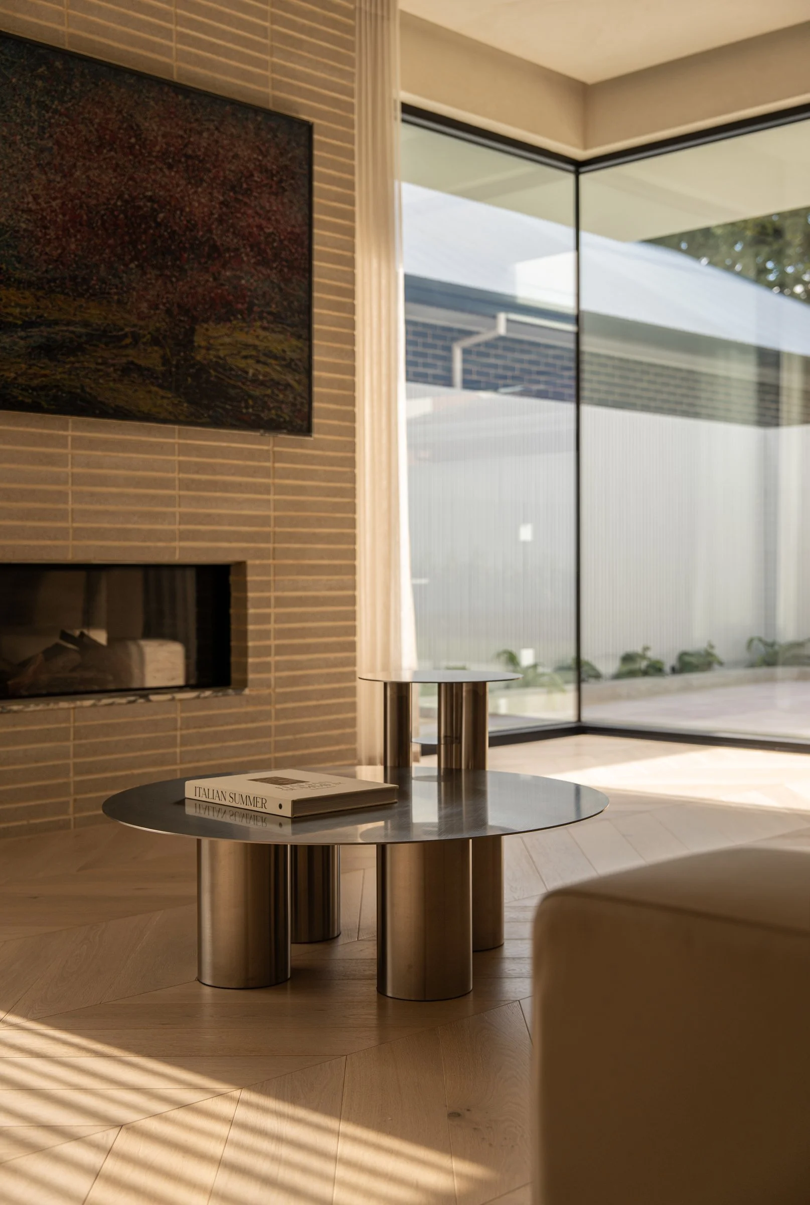 Round side table beside the brick fireplace and pool-facing windows in St Morris