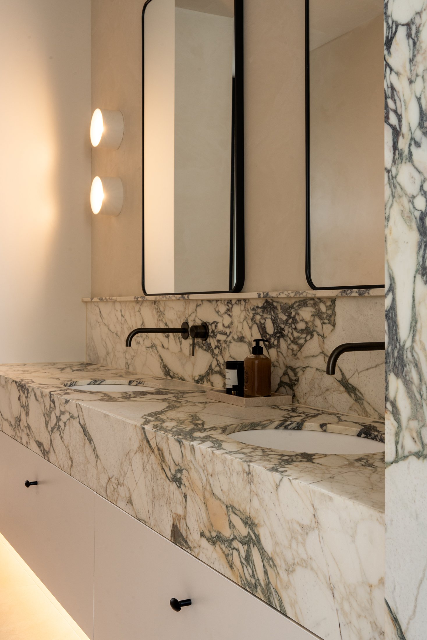 Veined stone bathroom vanity with twin mirrors and wall lights in St Morris