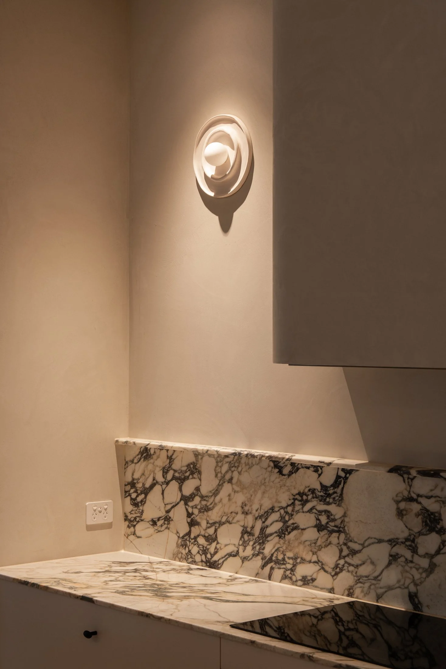 Decorative wall light above the veined kitchen stone splashback in St Morris