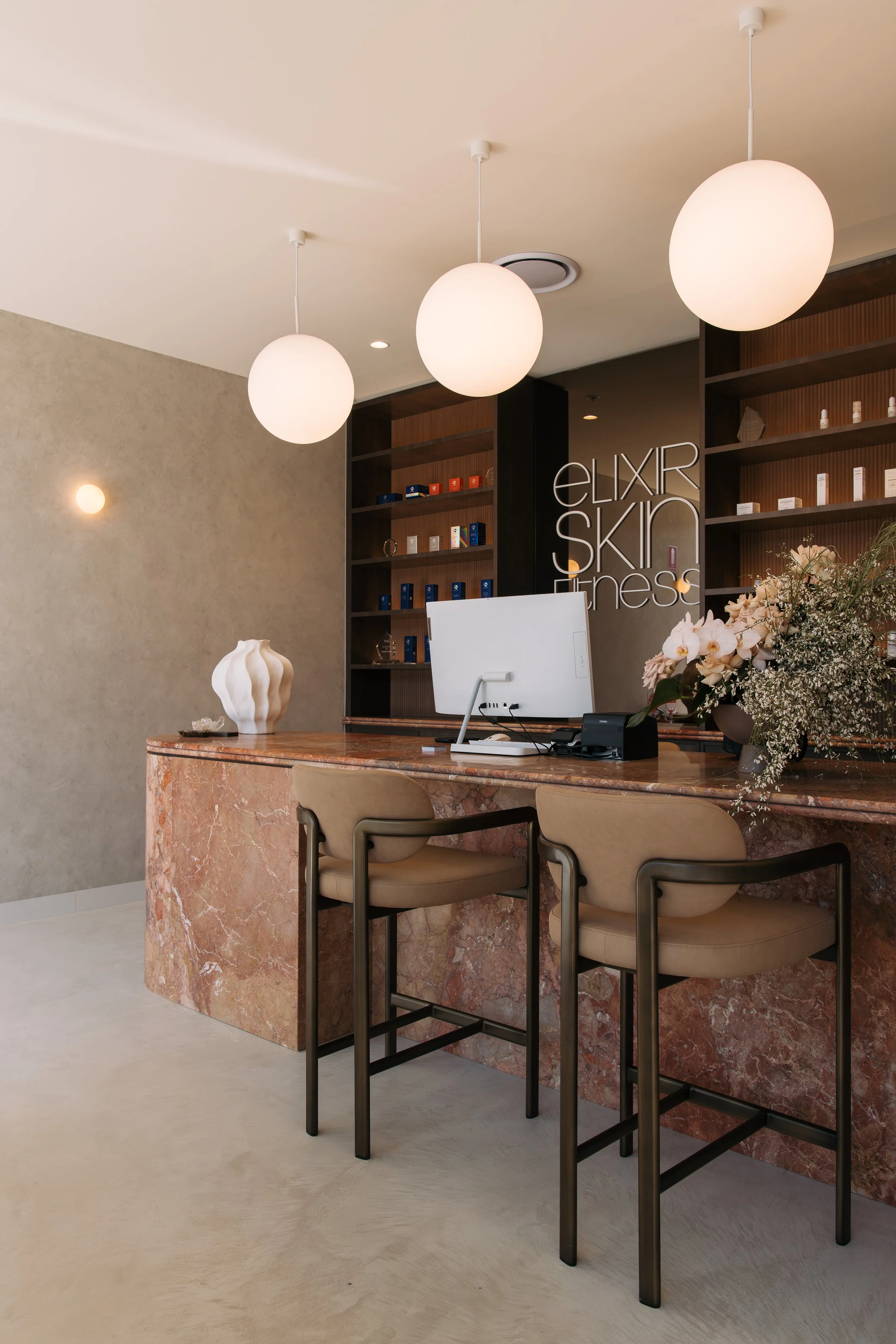 Curved marble reception desk with timber shelving and pendant lights at Elixir Skin Fitness