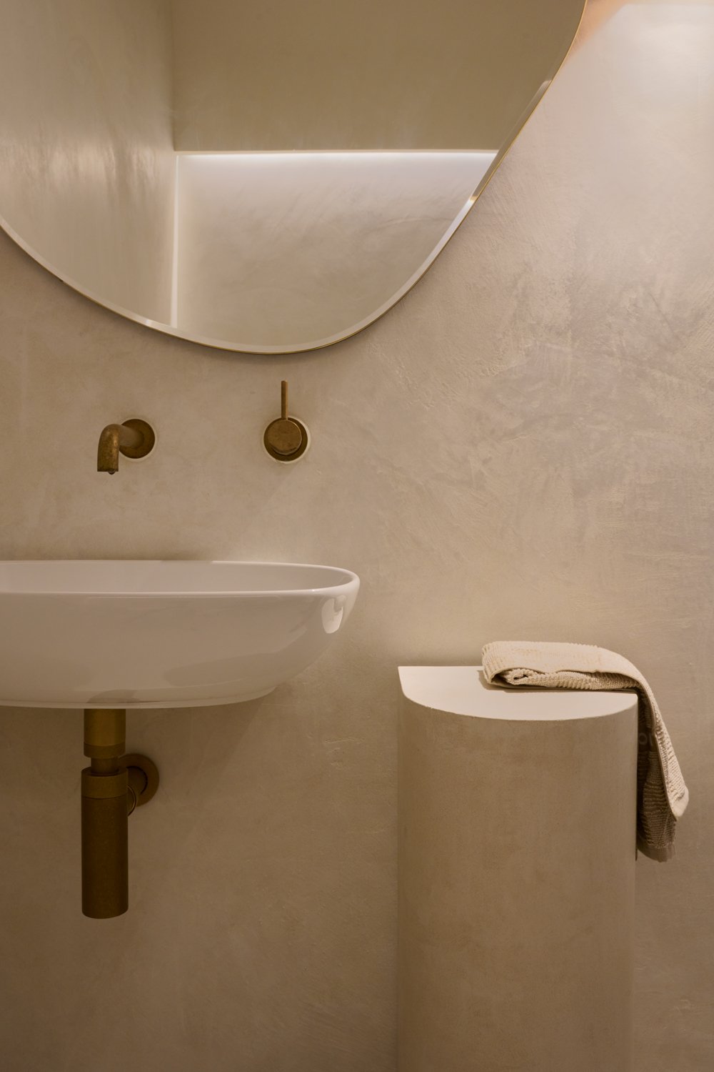Basin, brass wall taps and round mirror in the Sculpt Skin Clinic bathroom
