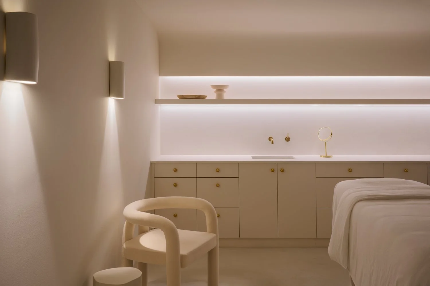 Treatment room with a pale chair, fitted cabinetry and wall-mounted taps at Sculpt Skin Clinic