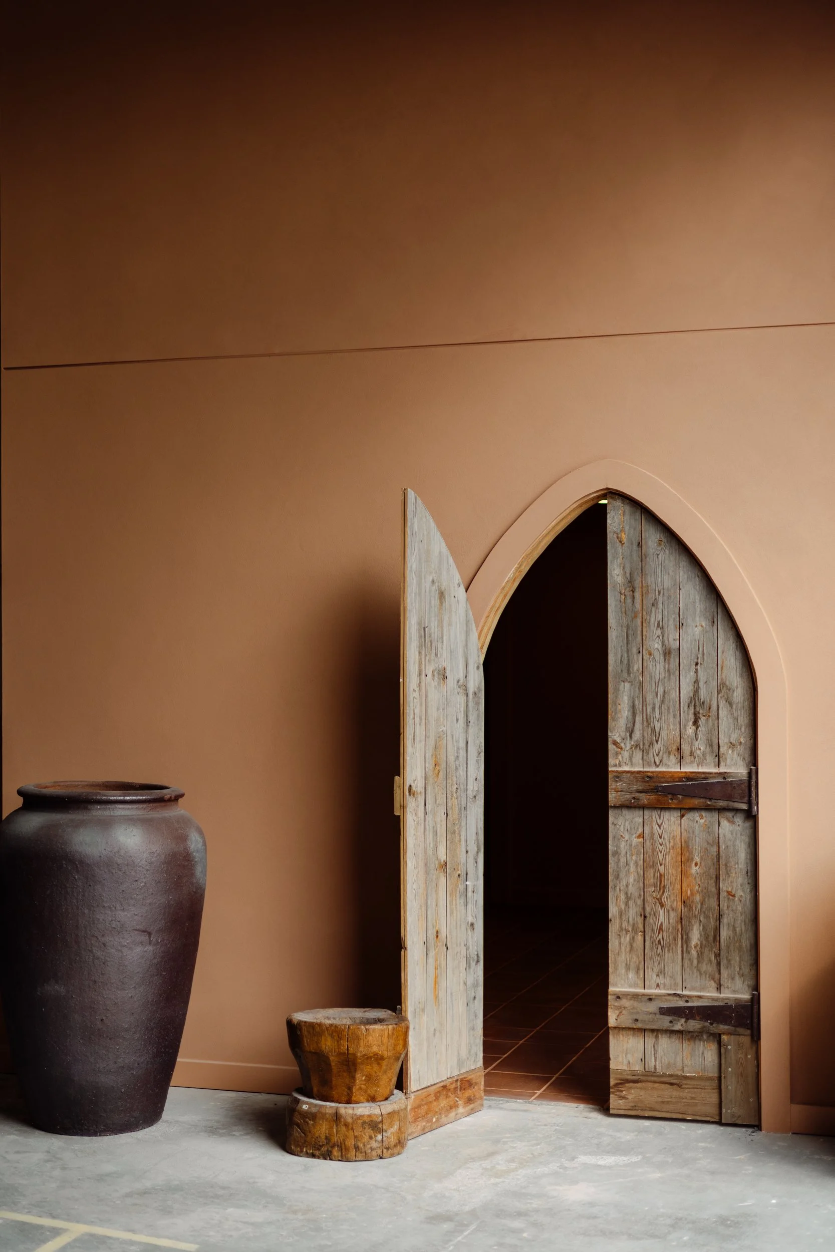 Rustic timber doors in a pointed archway set into terracotta walls at Stepney Warehouse
