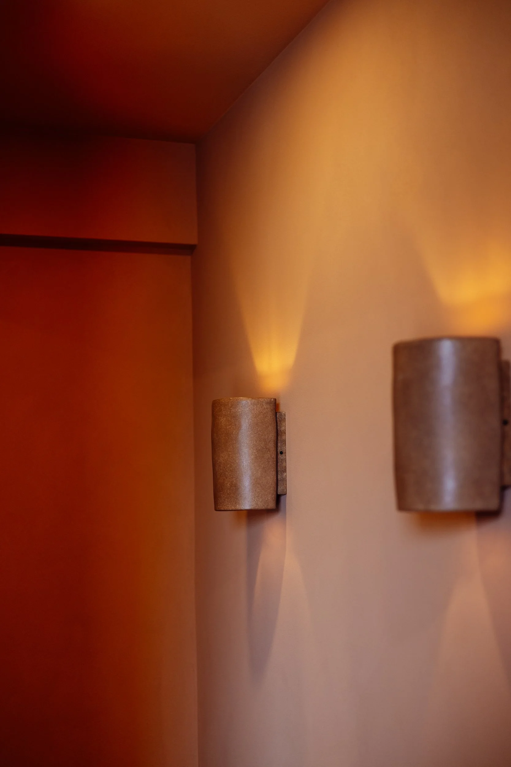 Pair of cylindrical wall lights casting warm light on terracotta render at Stepney Warehouse