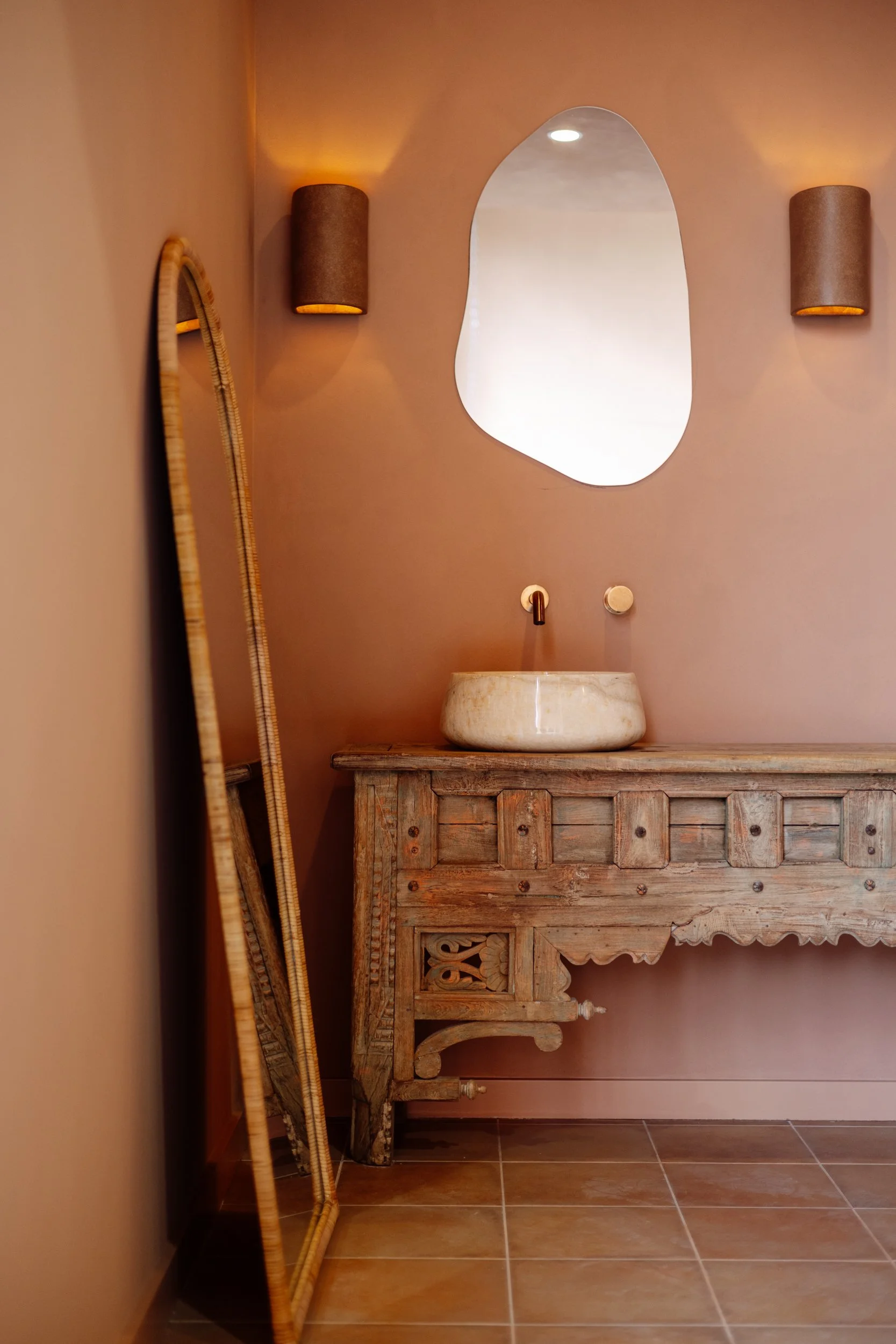 Carved timber vanity with a stone vessel basin and irregular mirror at Stepney Warehouse