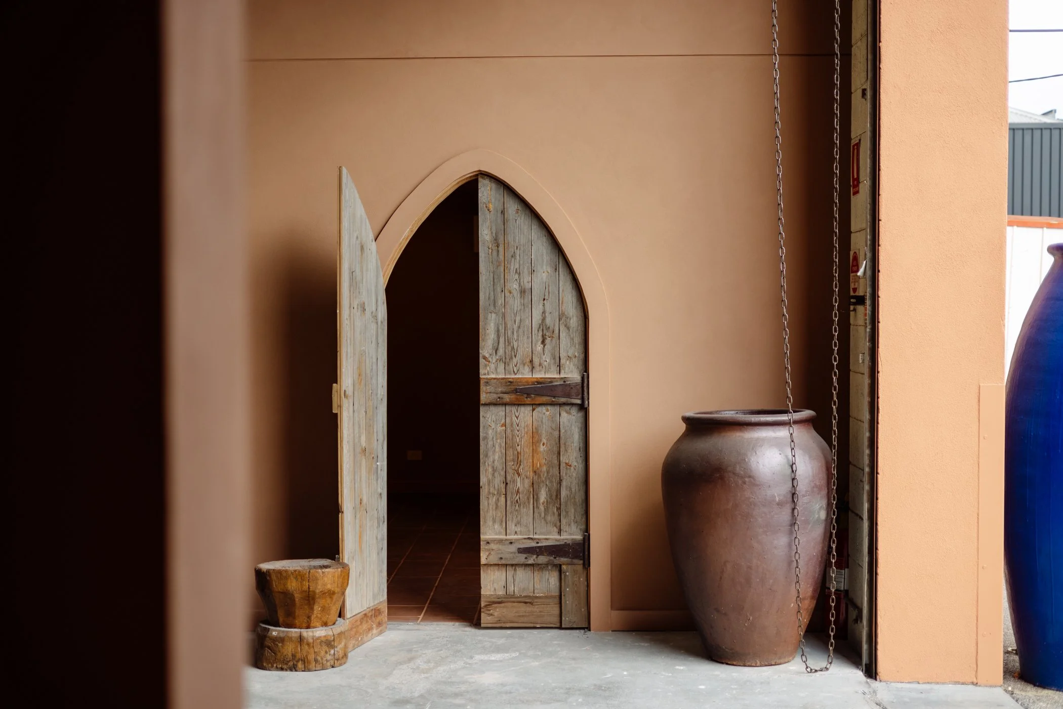 Rustic pointed-arch timber doors beside large ceramic vessels at Stepney Warehouse