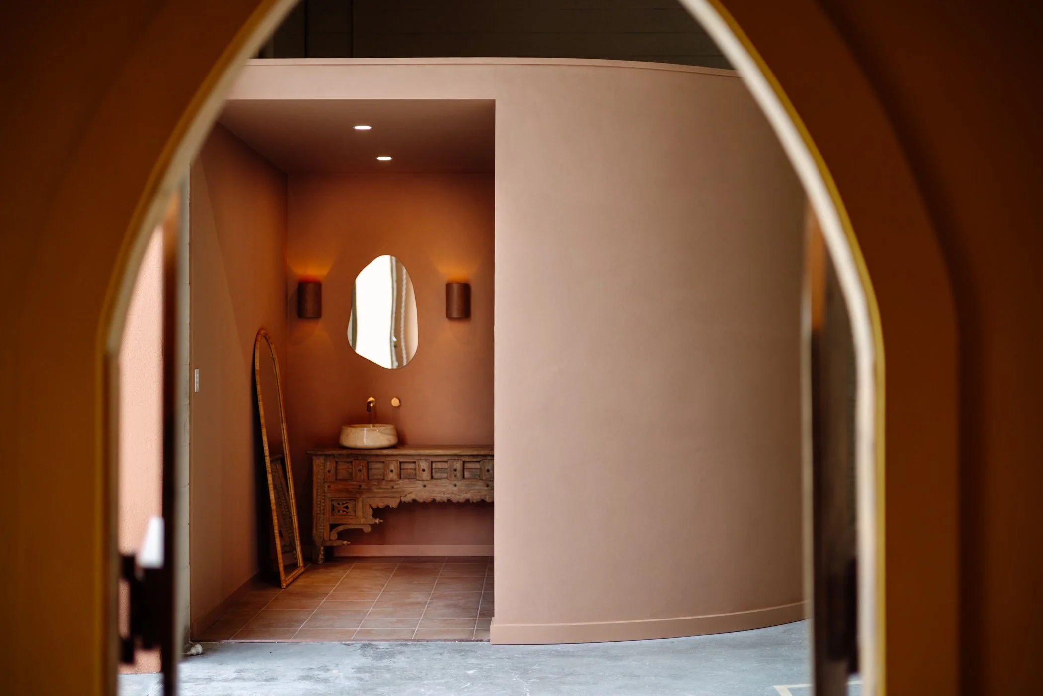 Arched opening framing the terracotta bathroom and timber vanity at Stepney Warehouse