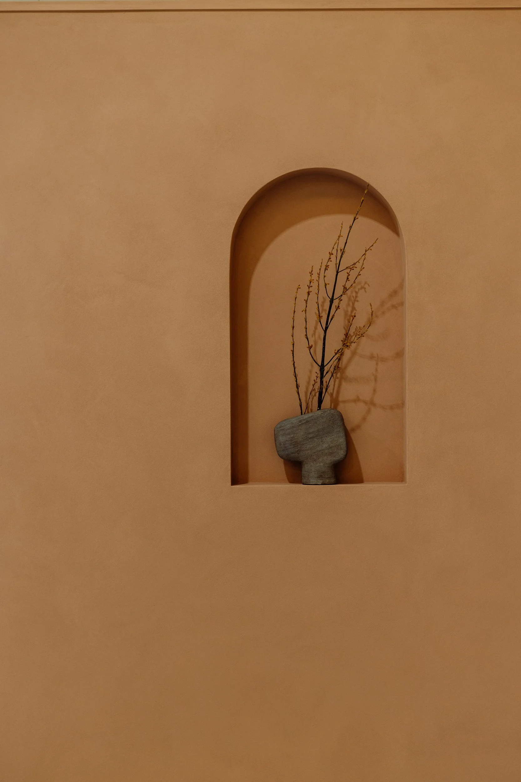 Arched wall niche holding a ceramic vase and branches at Stepney Warehouse